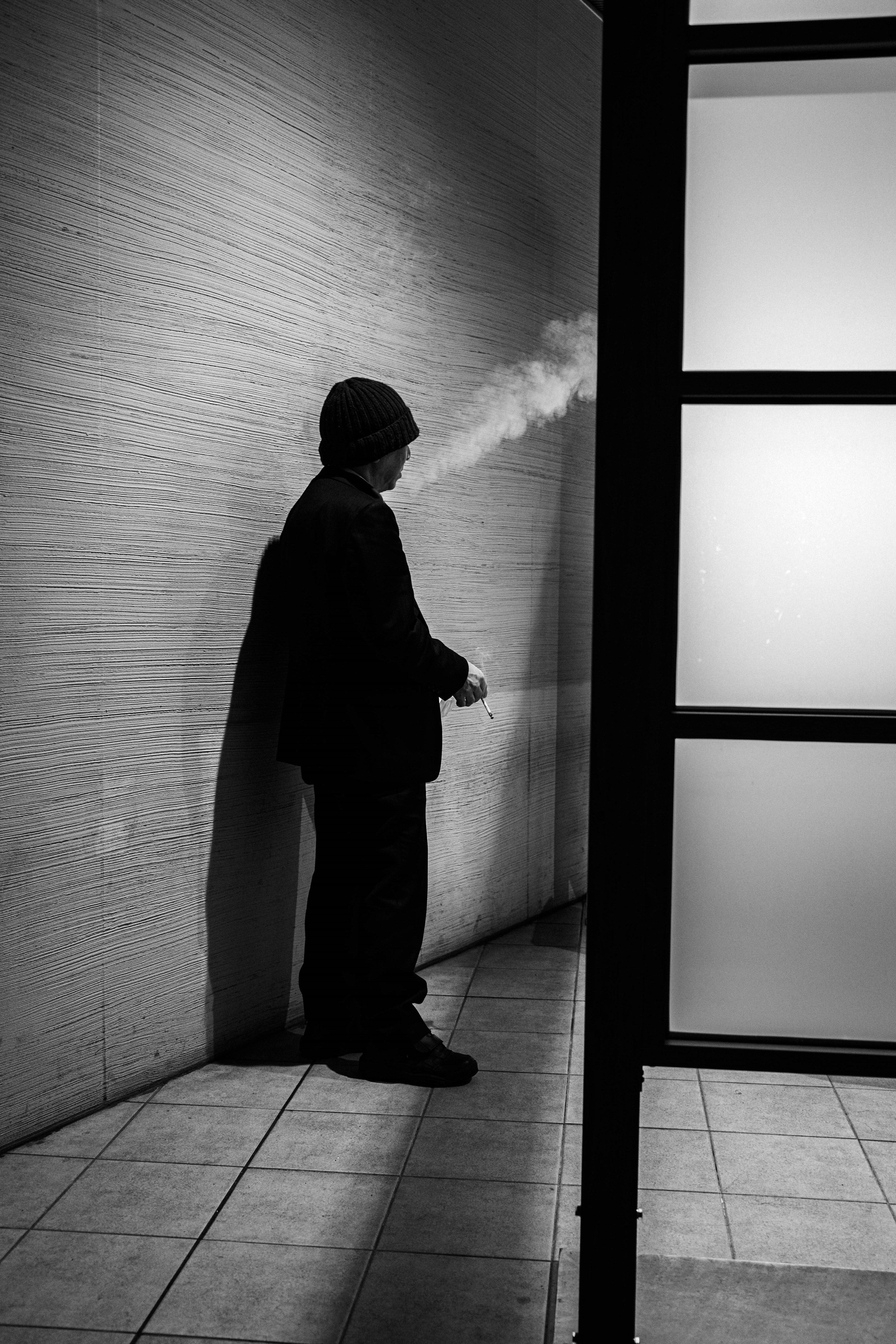 Silhouette di un uomo che fuma contro un muro in bianco e nero