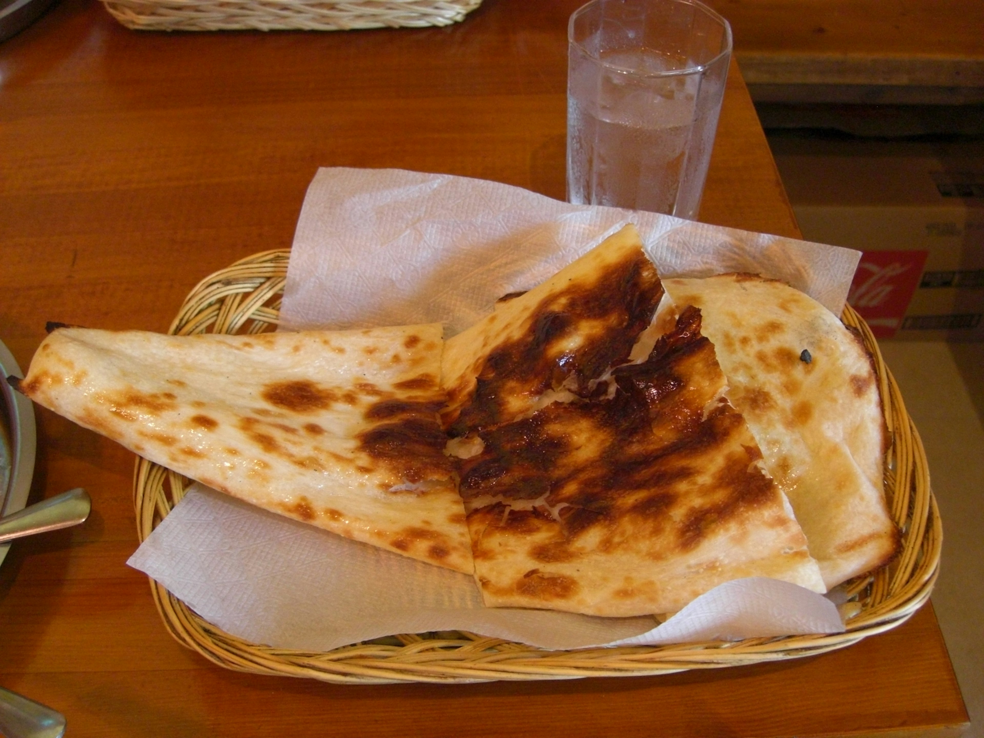 Un pane naan croccante servito in un cestino intrecciato con un bicchiere d'acqua sullo sfondo