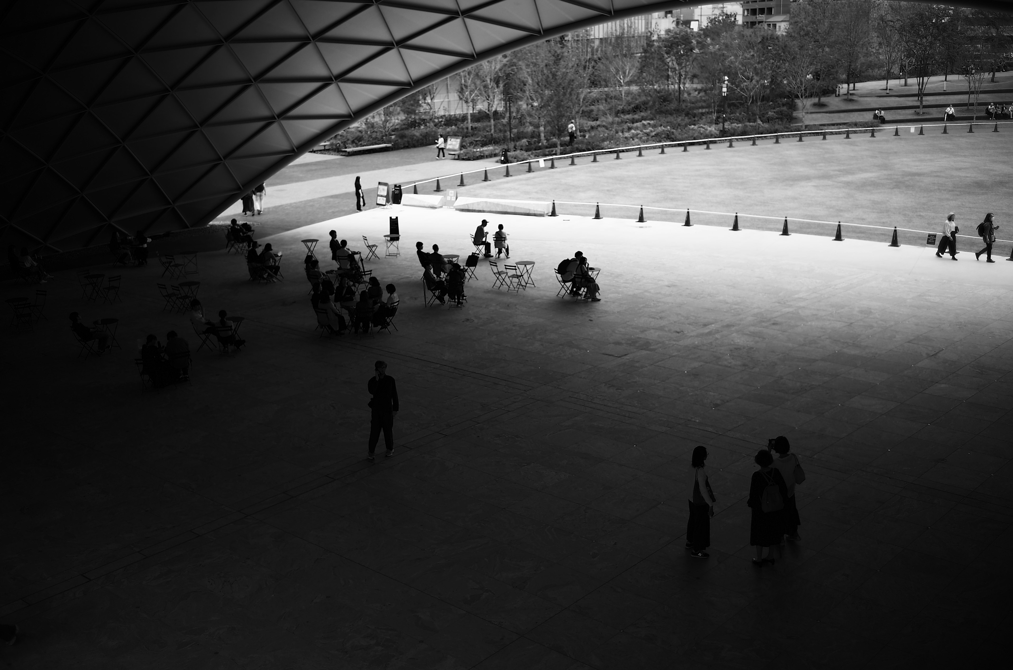 Black and white scene of people gathering in an outdoor space featuring a large arching roof