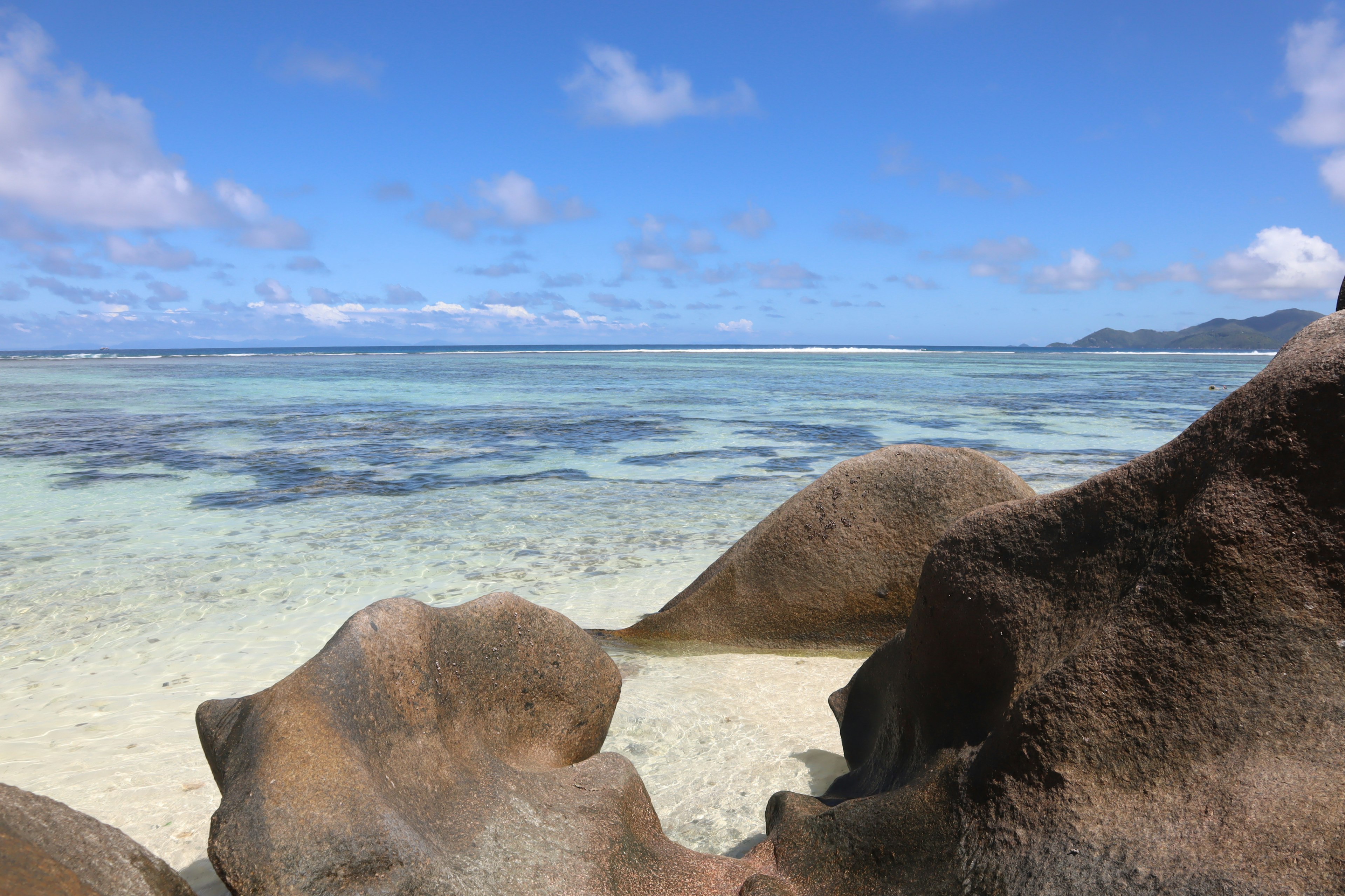 Batu besar dengan lautan biru jernih dan langit di latar belakang