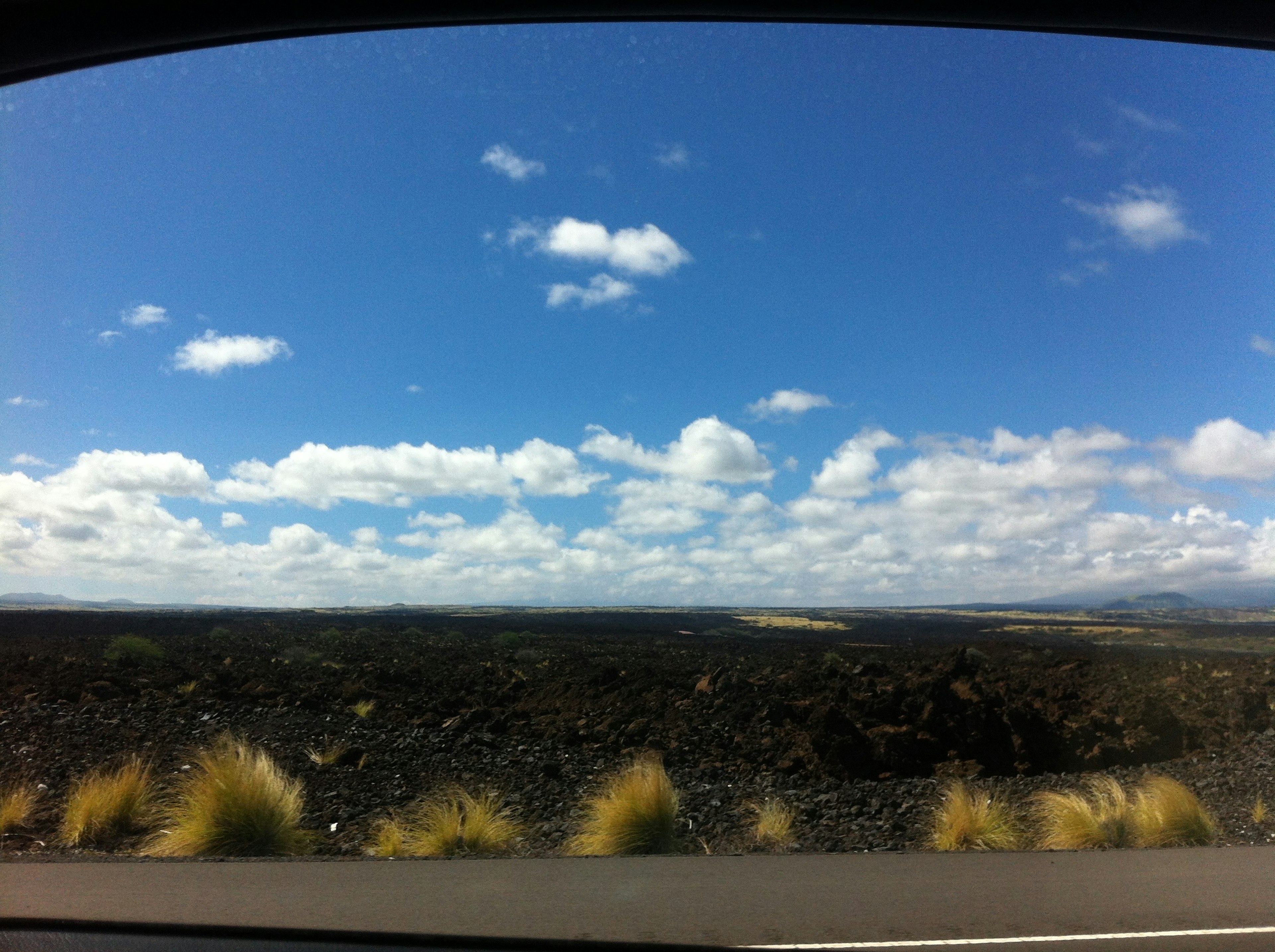 Scenic view of blue sky with white clouds over black lava landscape and grass