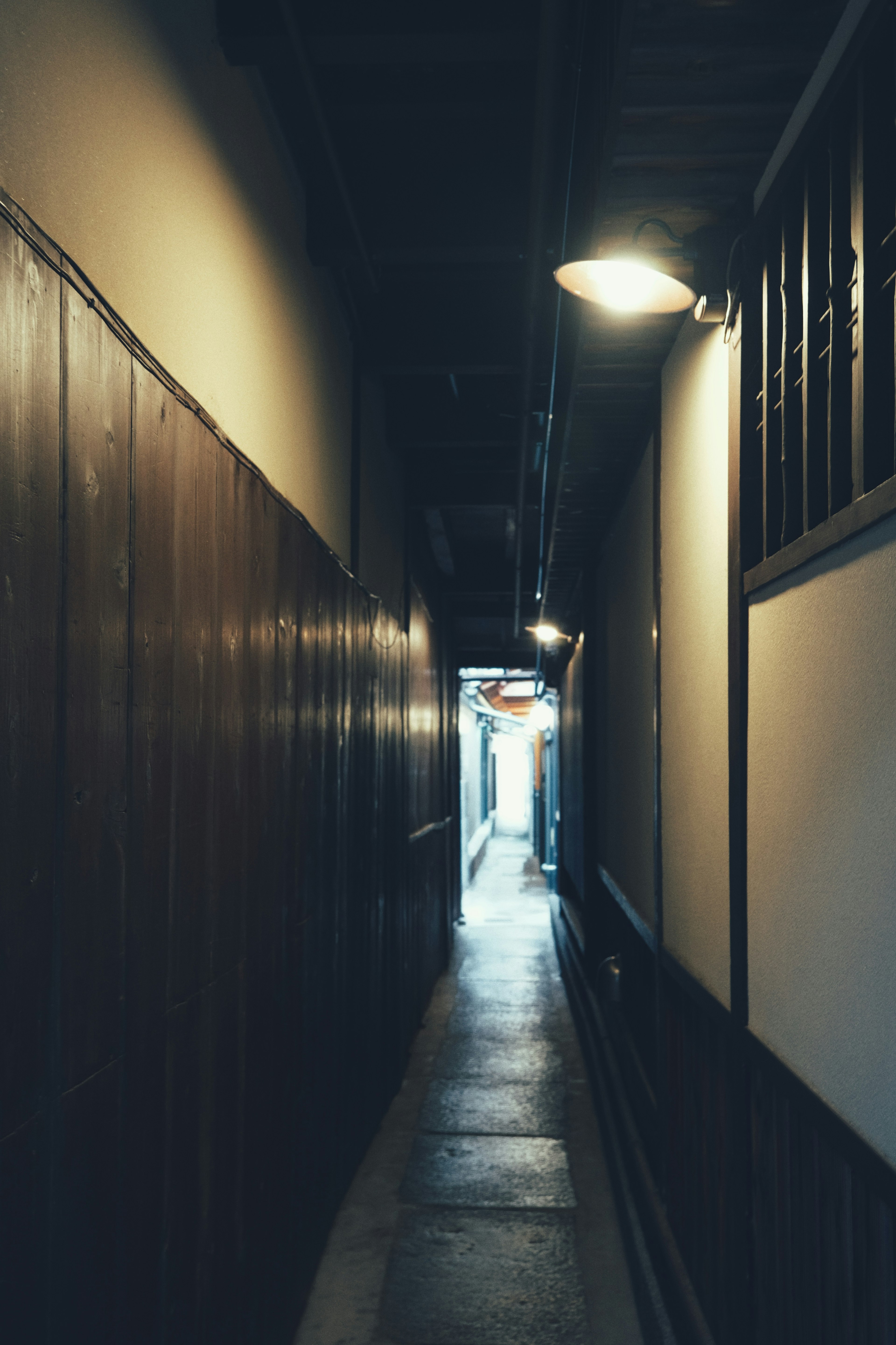 Un couloir étroit avec des murs en bois et un éclairage doux menant à une sortie lumineuse