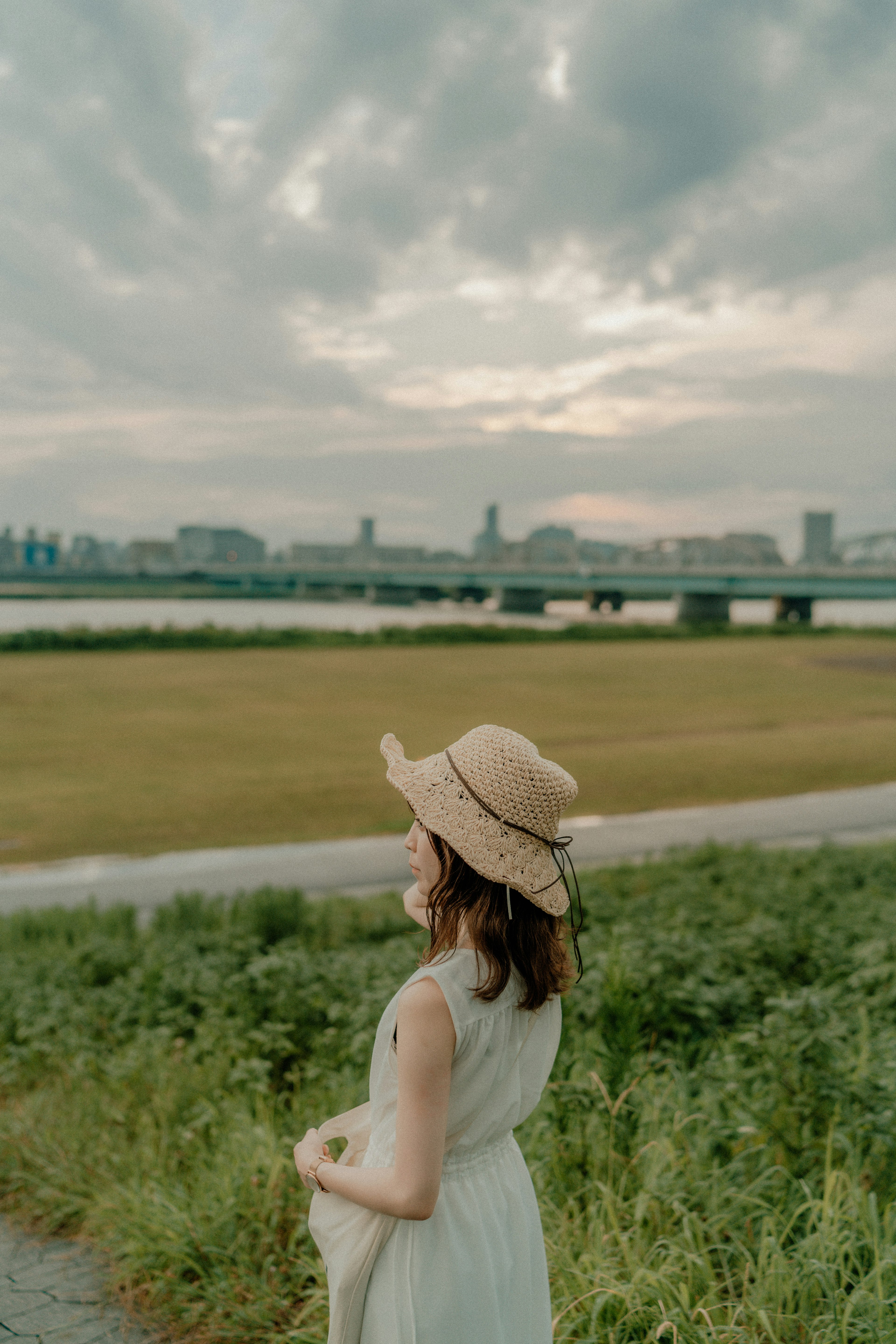 女性が麦わら帽子をかぶり、川の岸辺で立っている風景