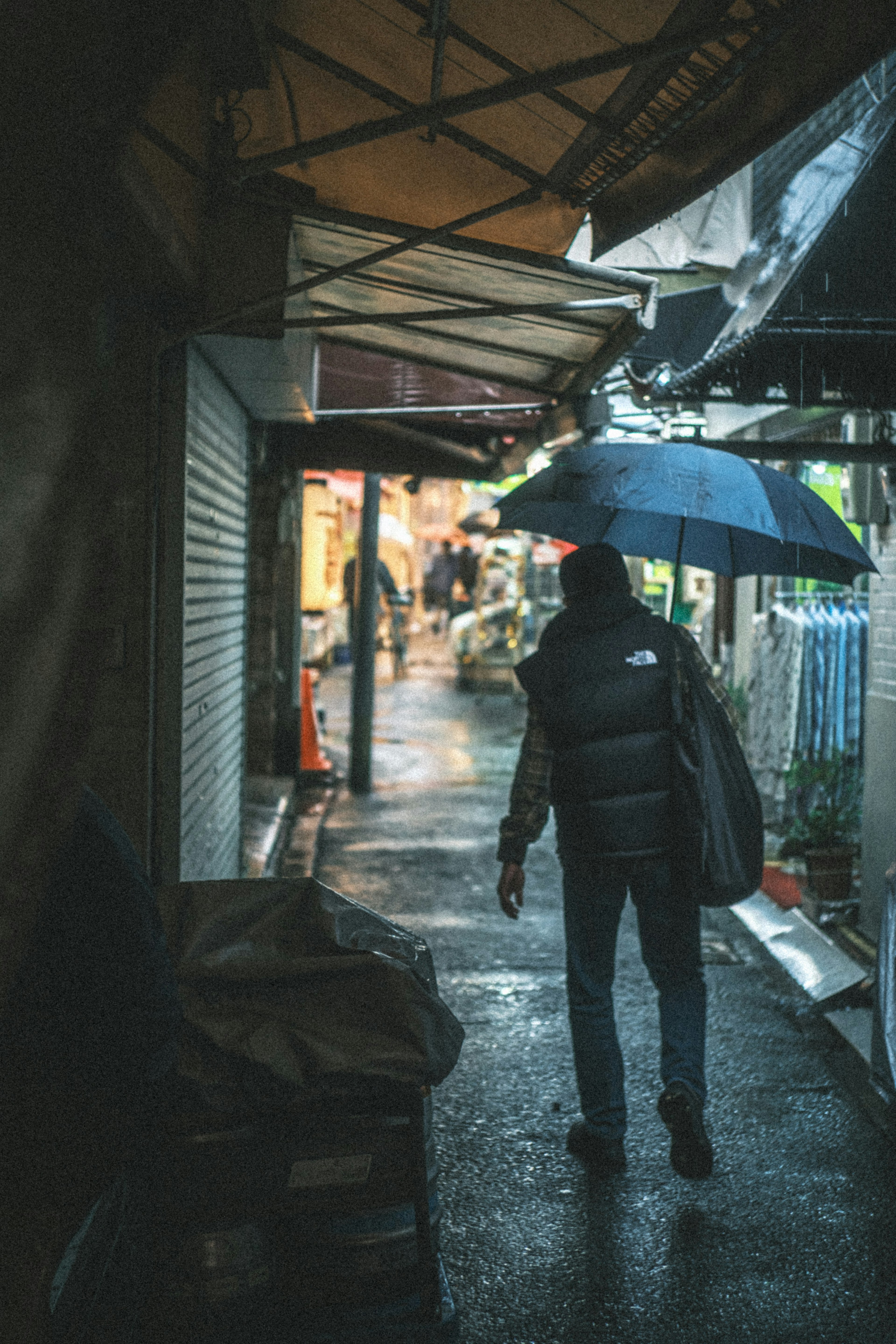 A person walking with an umbrella in the rain along a narrow street