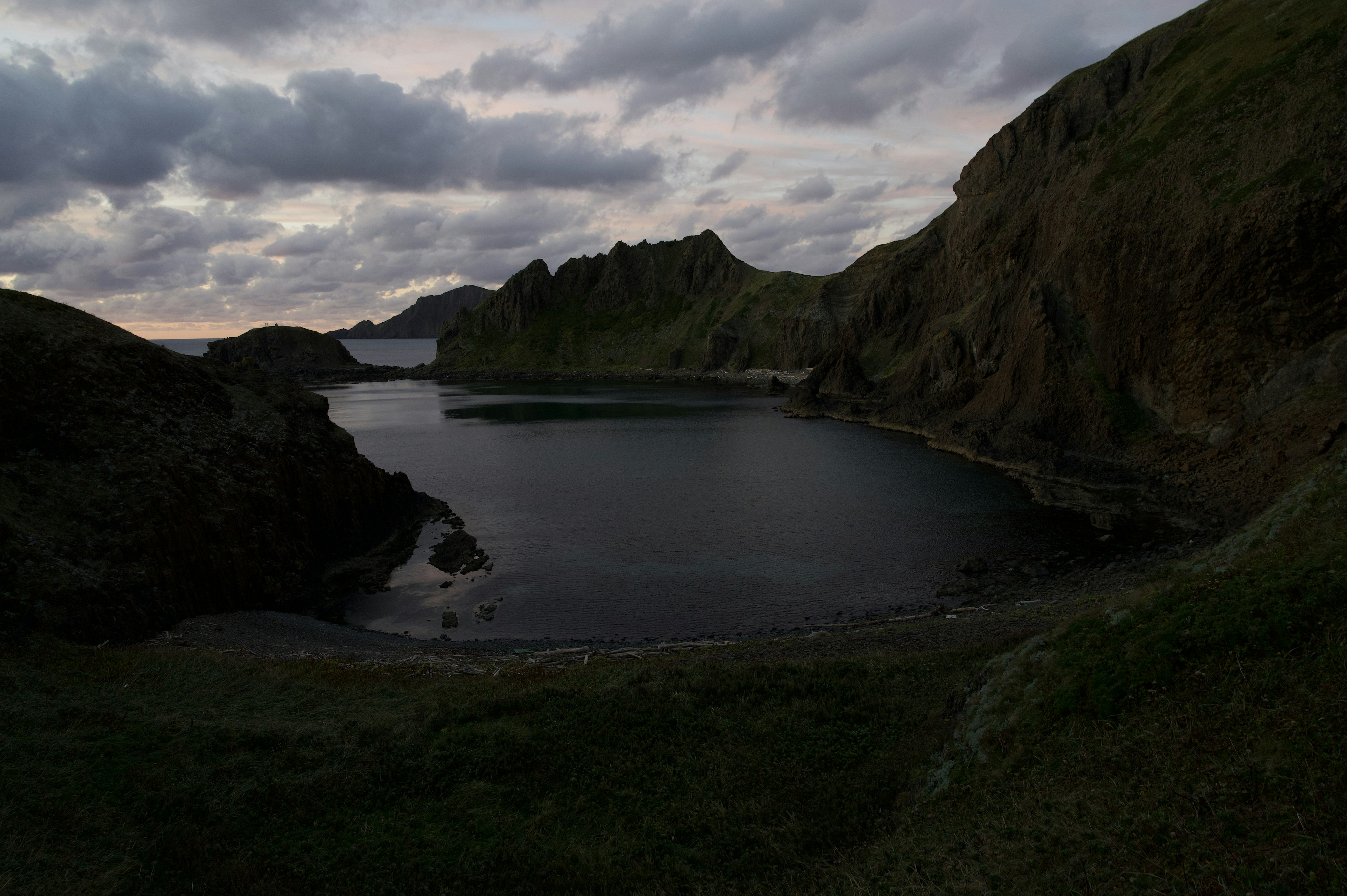 Paysage côtier sombre avec des collines rocheuses et une surface d'eau calme sous un ciel nuageux