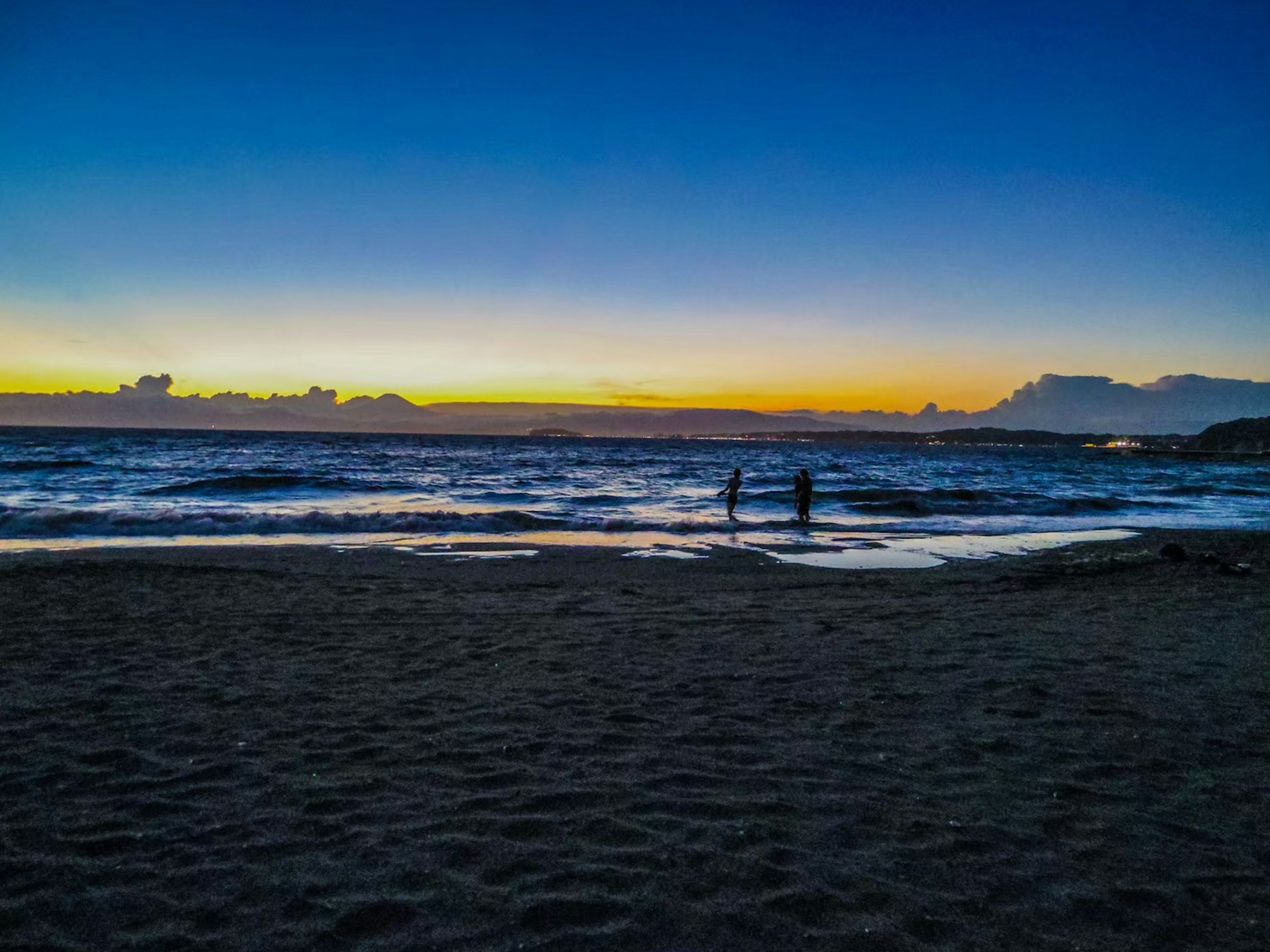 Orang-orang menikmati pantai saat matahari terbenam dengan langit berwarna-warni