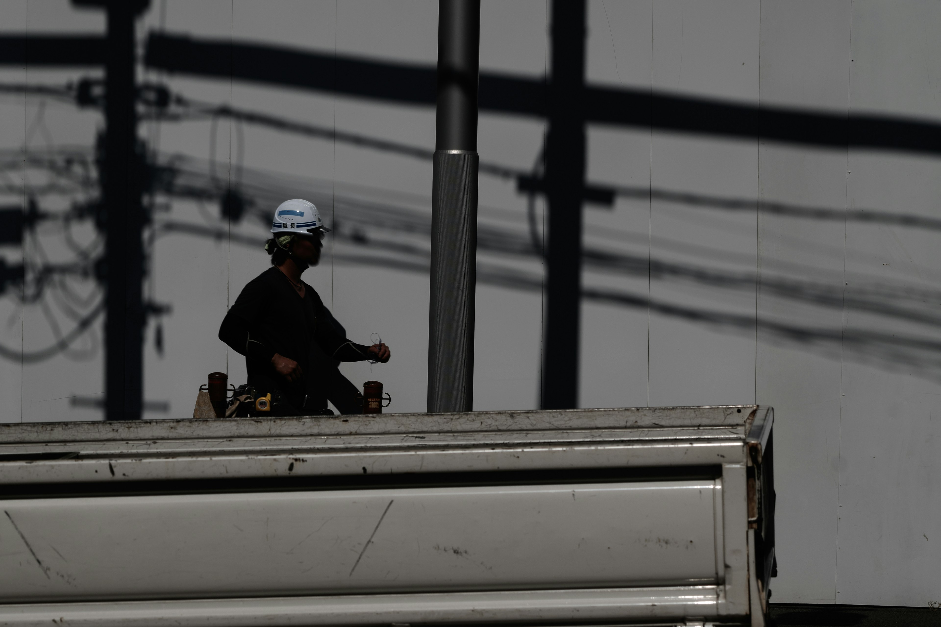 Arbeiter steht auf einem Gebäude mit schattierten Stromleitungen