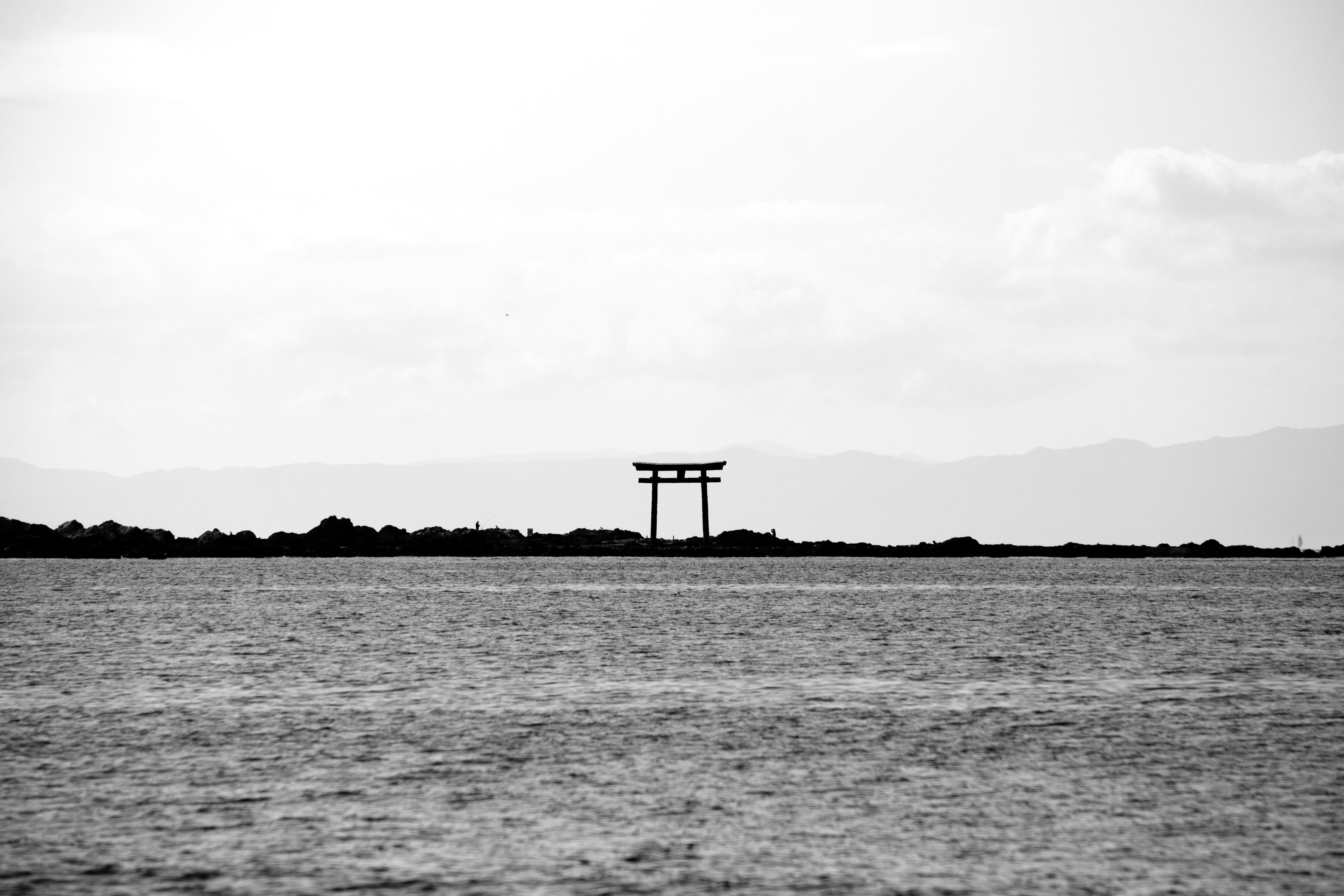 海に浮かぶ鳥居のシルエットと遠くの山々