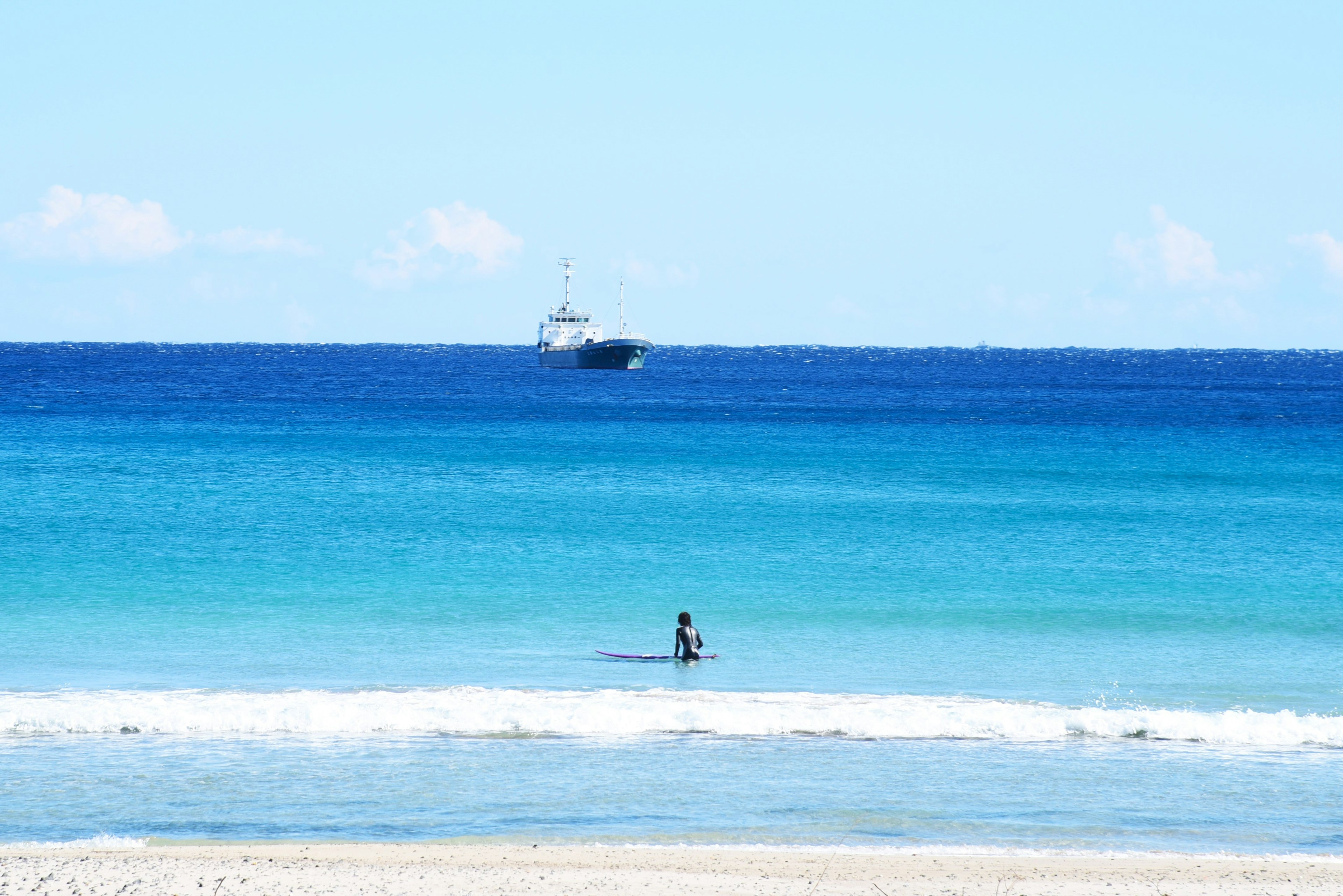 青い海と空の下でサーフィンを楽しむ人と遠くの船