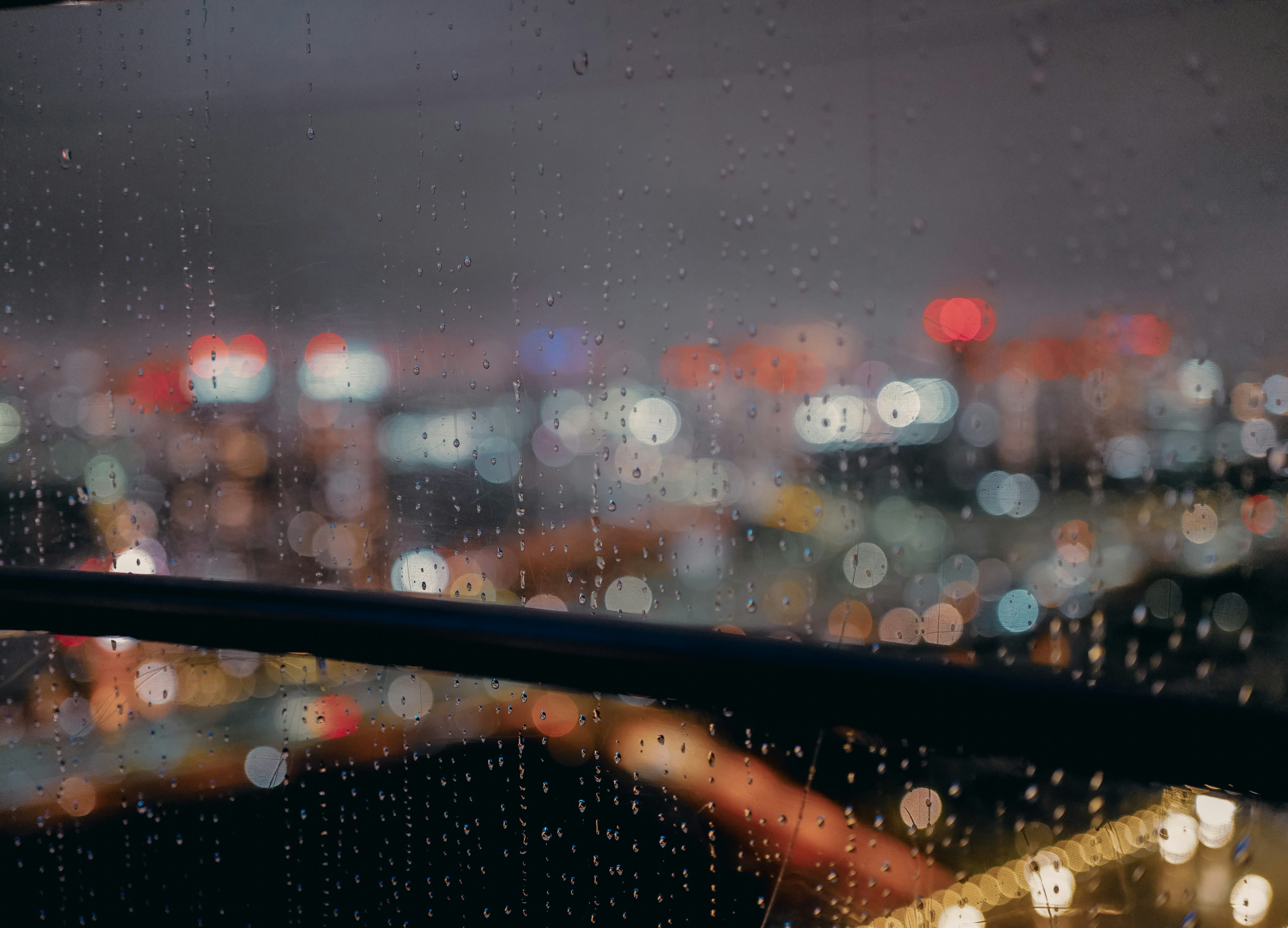 雨滴がついた窓越しにぼんやりとした都市の夜景が広がる