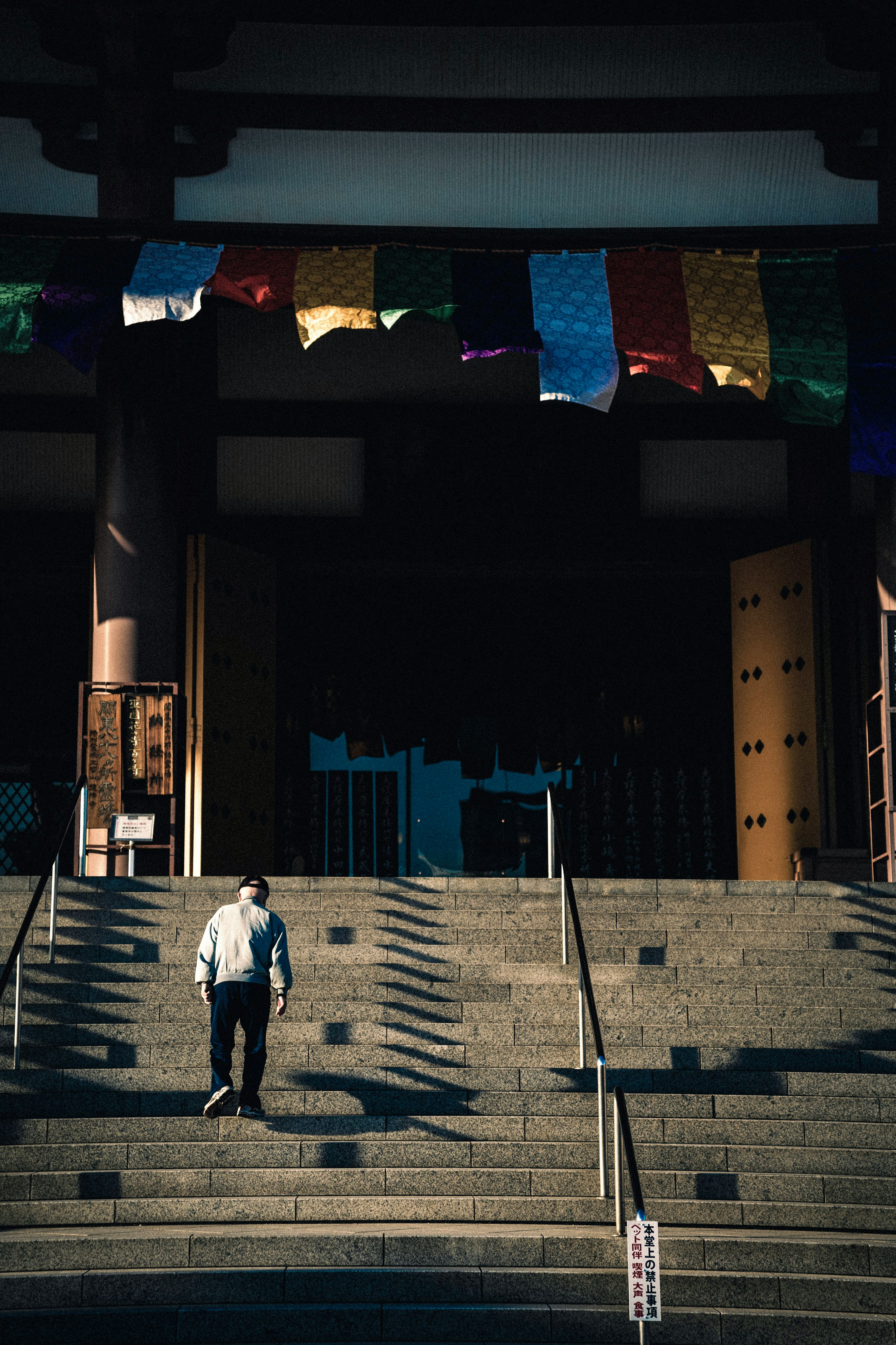 Persona bajando escaleras en la entrada de un templo con banderas de oración coloridas colgando