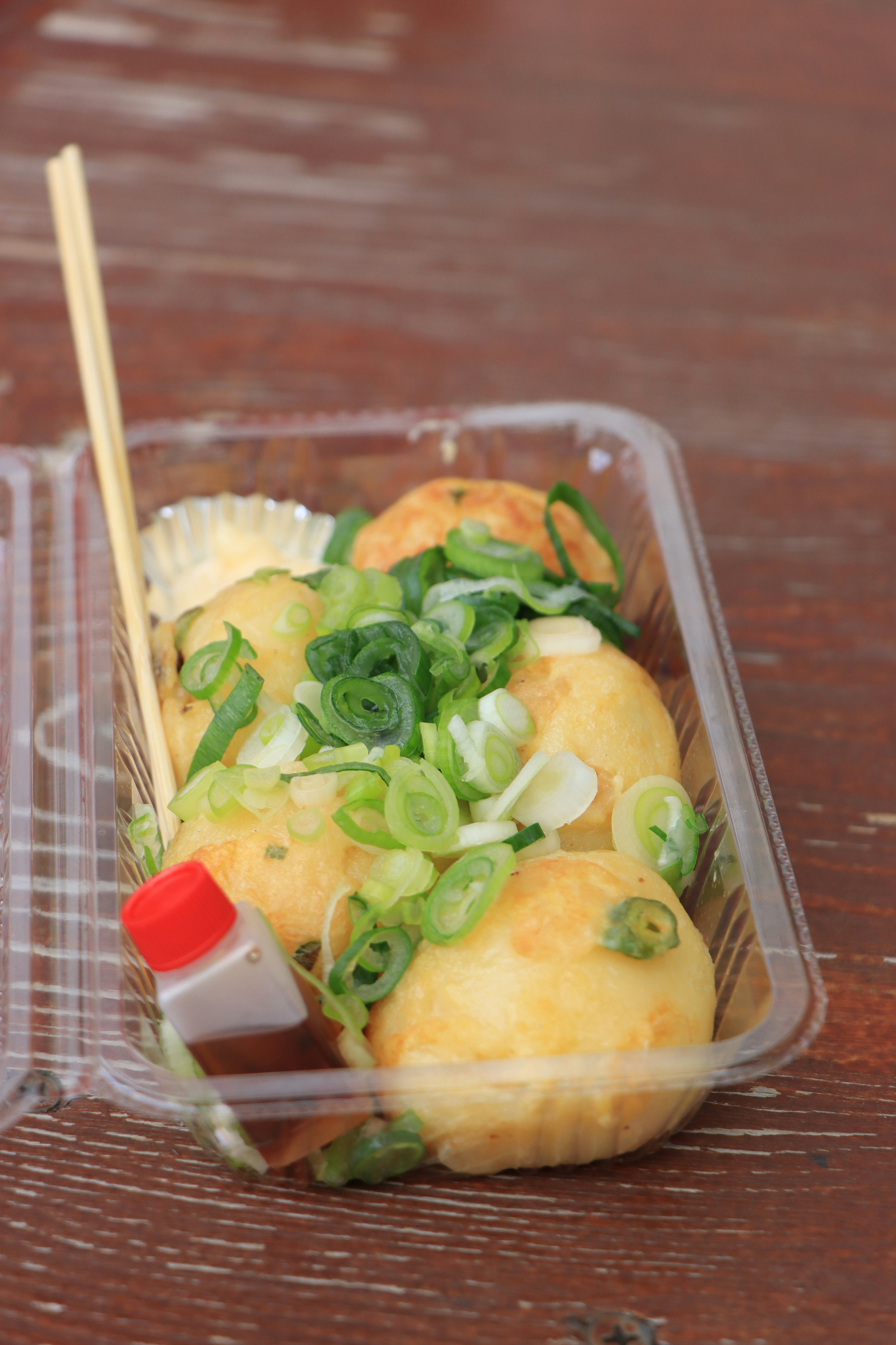 Takoyaki serviert mit Frühlingszwiebeln und Sauce in einem Behälter