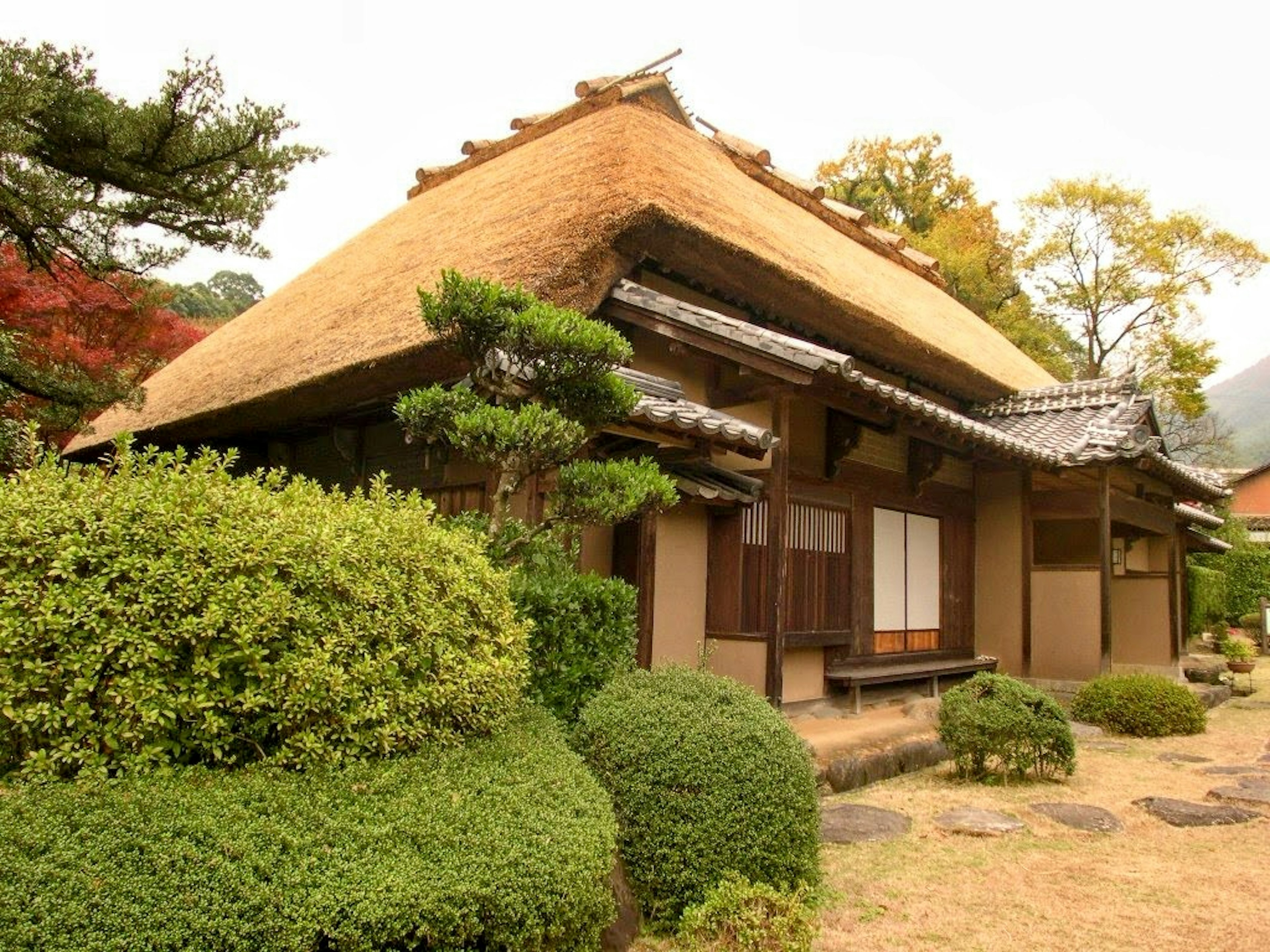 Traditional Japanese house exterior with thatched roof and lush green garden