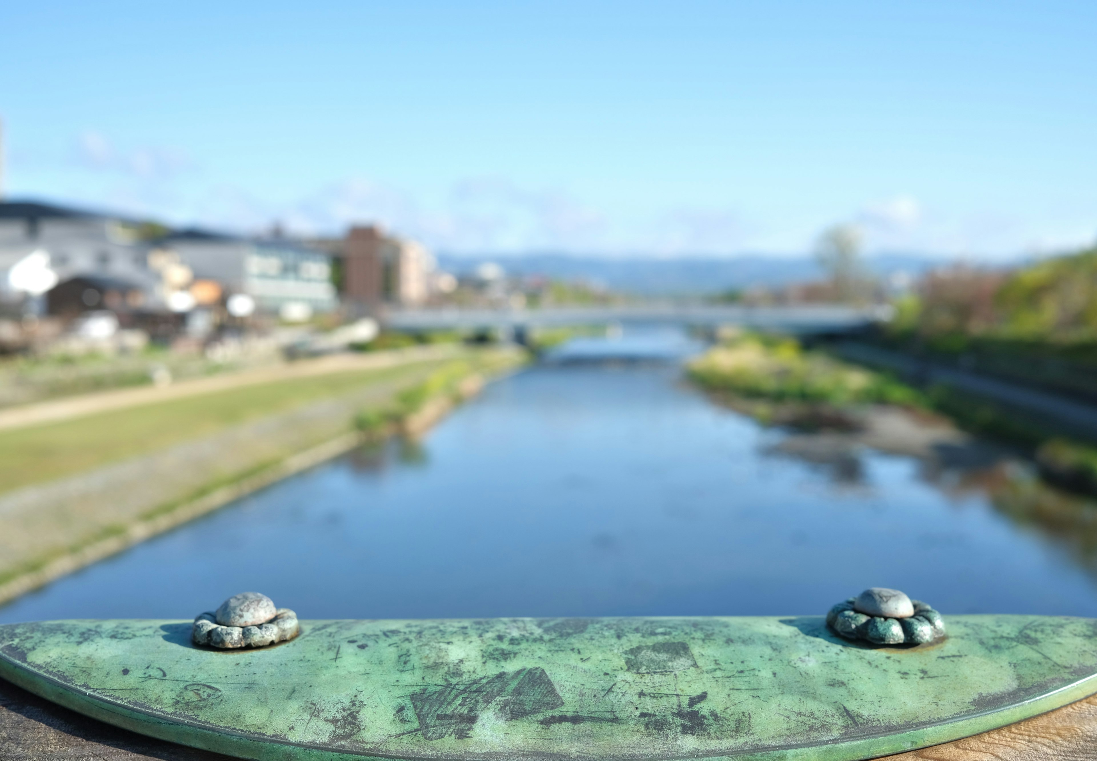 Vista escénica de un río y un puente con una barandilla de bronce en primer plano y cielo azul al fondo