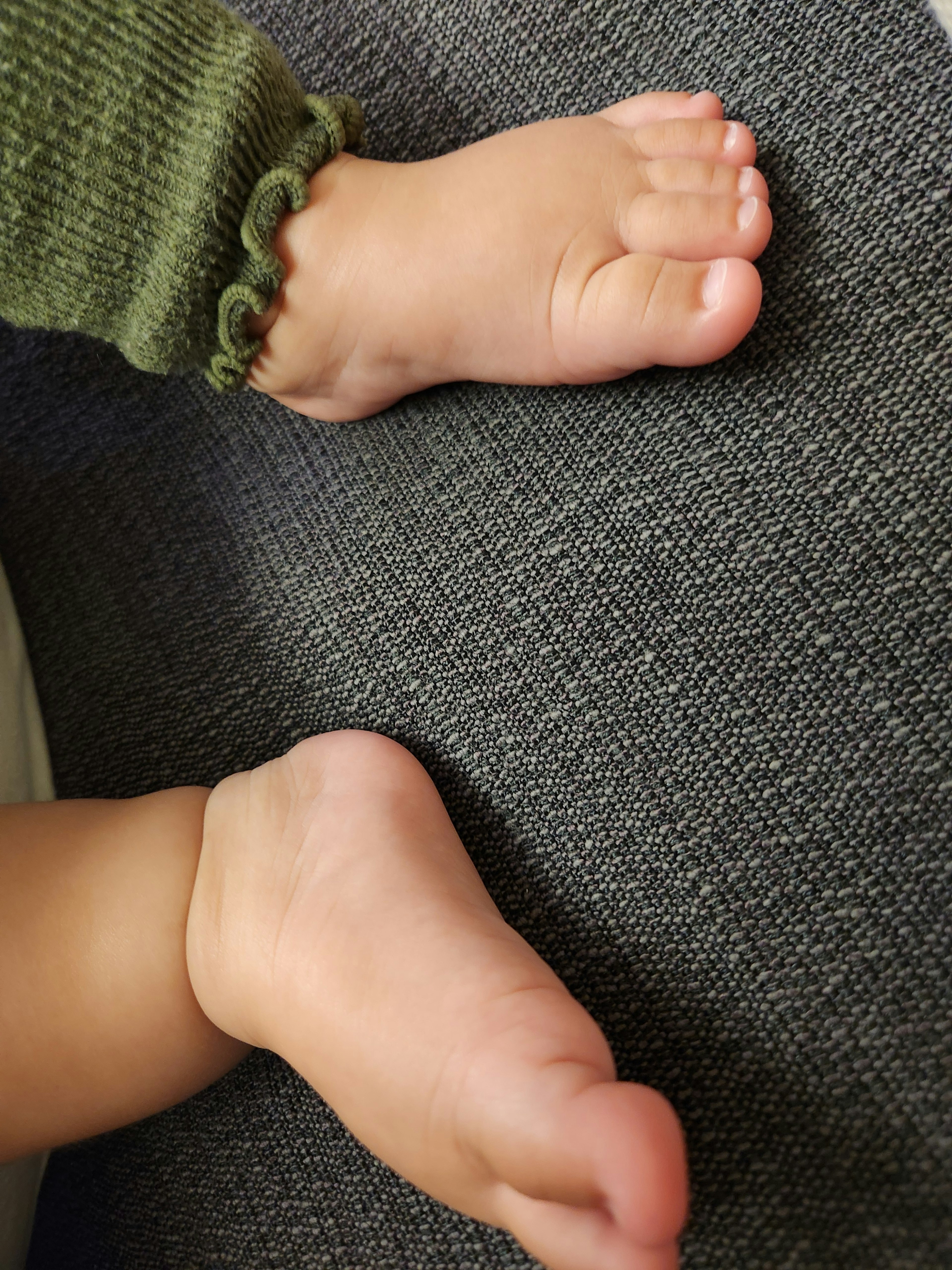 Deux pieds de bébé reposant sur une surface grise texturée avec une manche en tricot vert visible