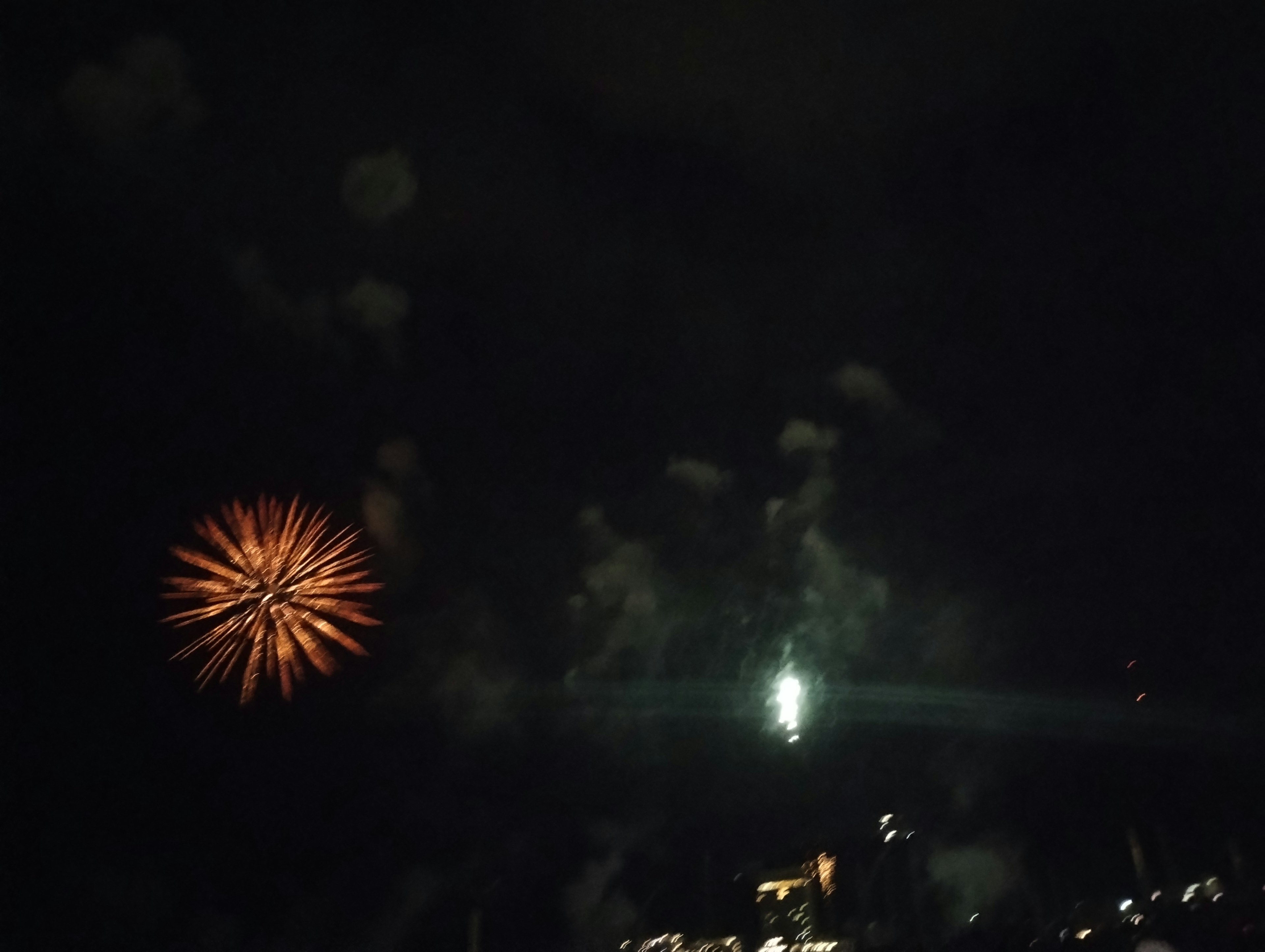 Espectáculo de fuegos artificiales en el cielo nocturno con explosiones naranjas y blancas