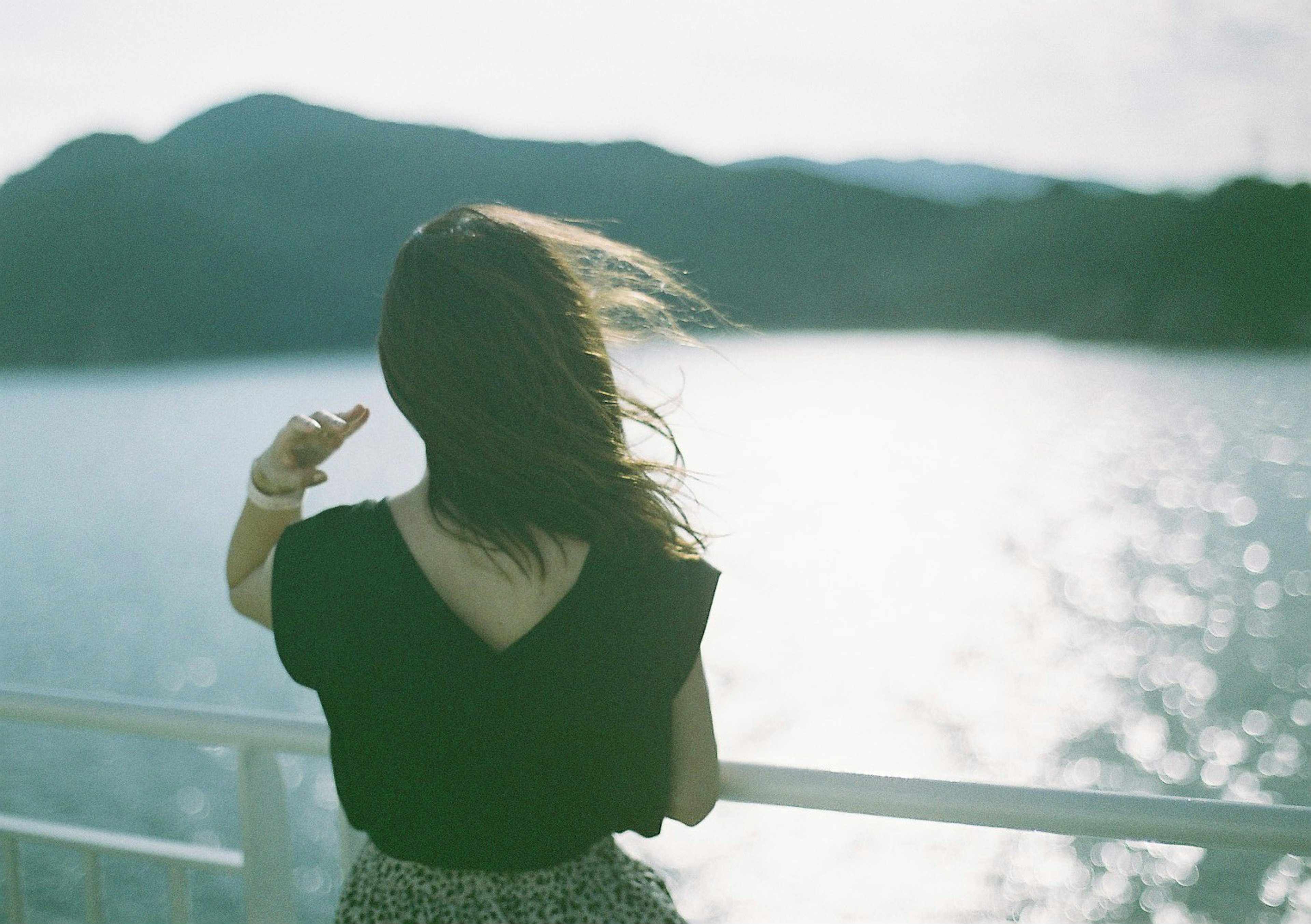 A woman standing with her back to the sea Hair fluttering in the wind Soft evening light