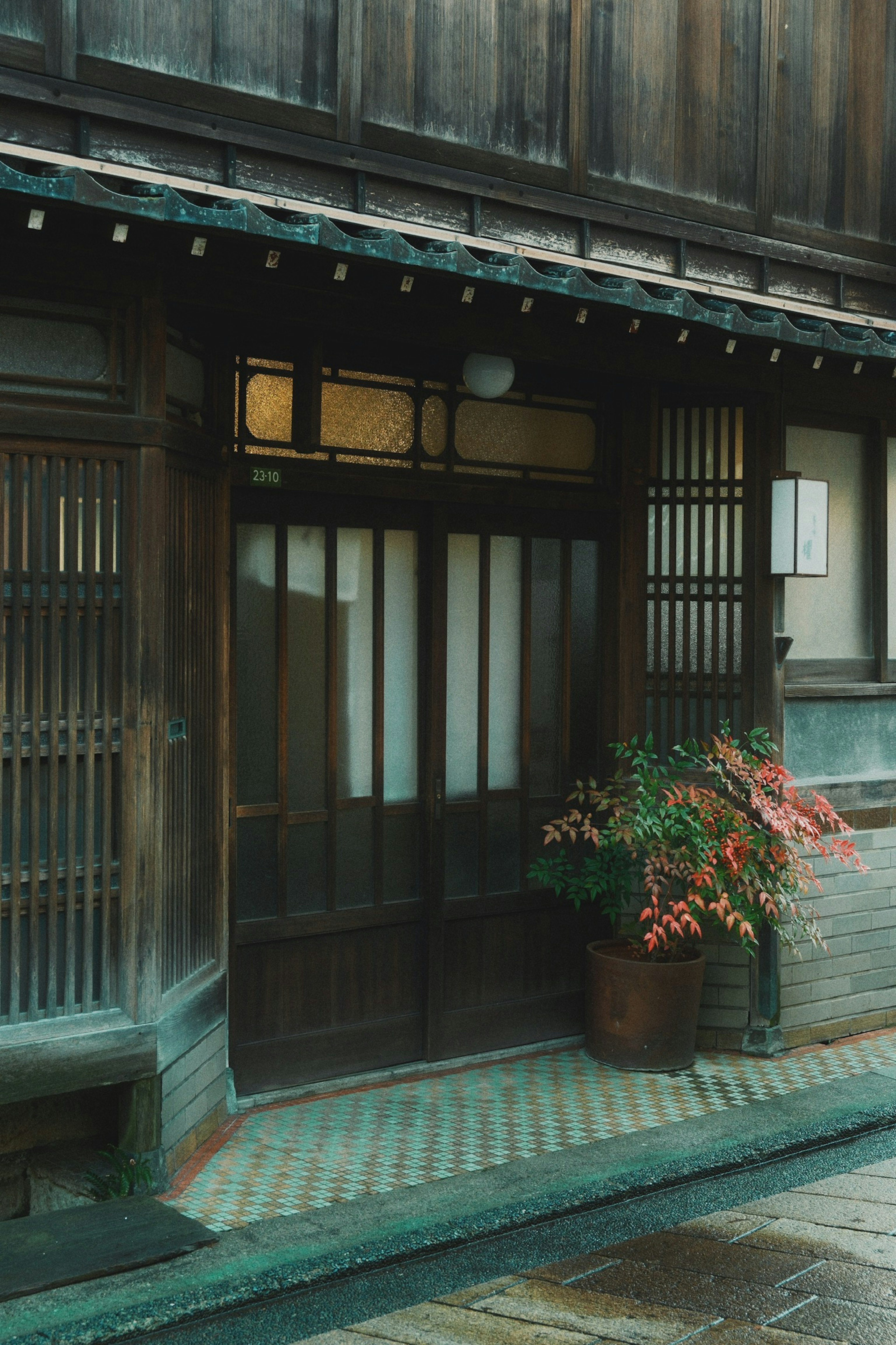 Pintu masuk rumah tradisional Jepang dengan pintu kayu dan jendela kisi dengan bunga dalam pot