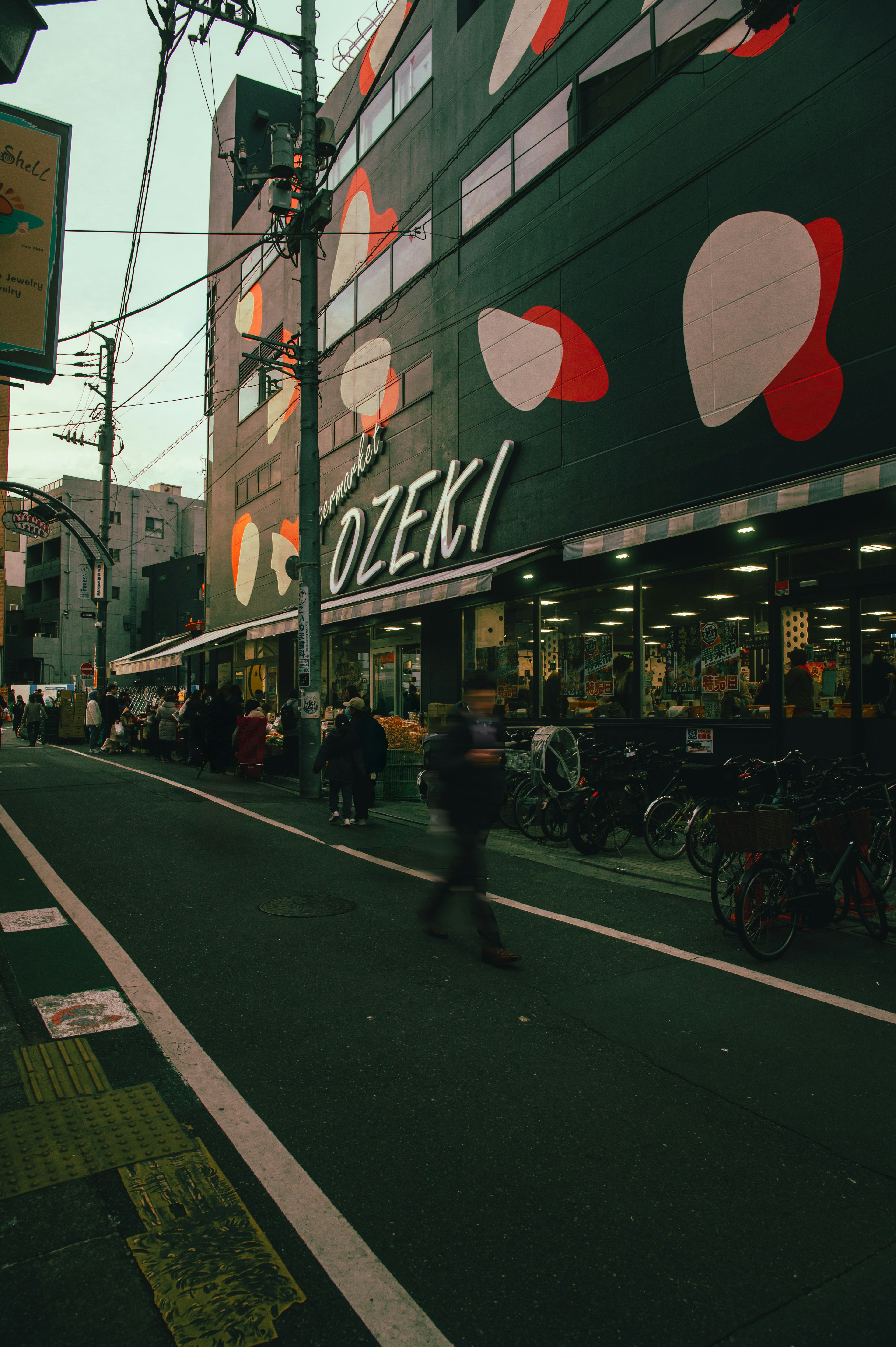 Ozekiの店舗が描かれた街並みの画像 自転車が並び 色とりどりの模様が施された建物