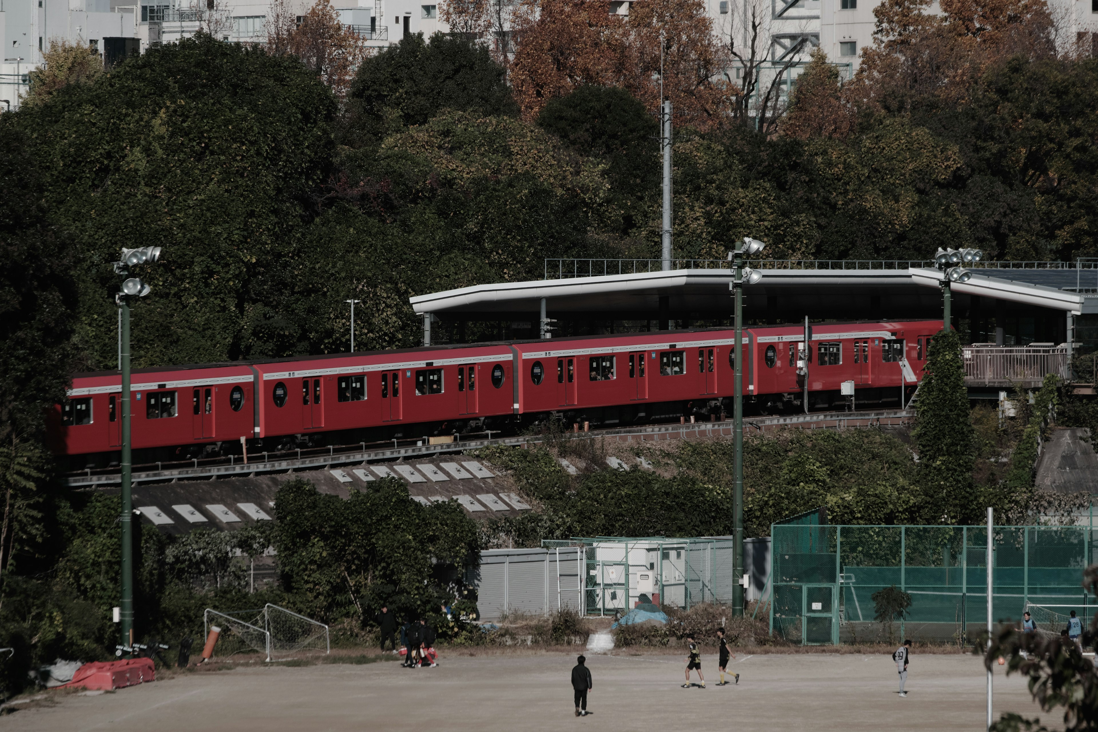 Tren rojo atravesando una vía elevada cerca de un parque con personas