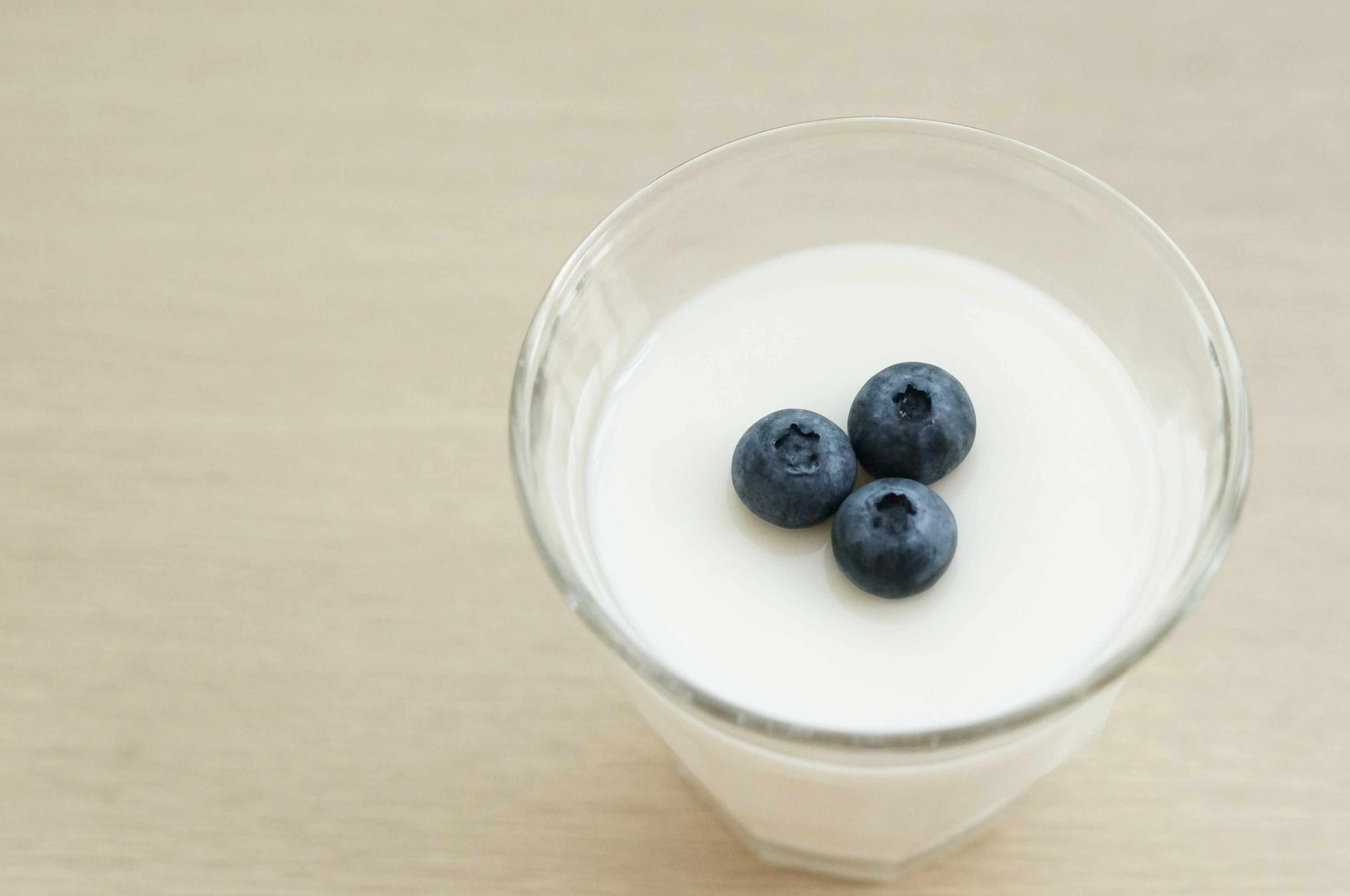 Un vaso de yogur cremoso cubierto con tres arándanos