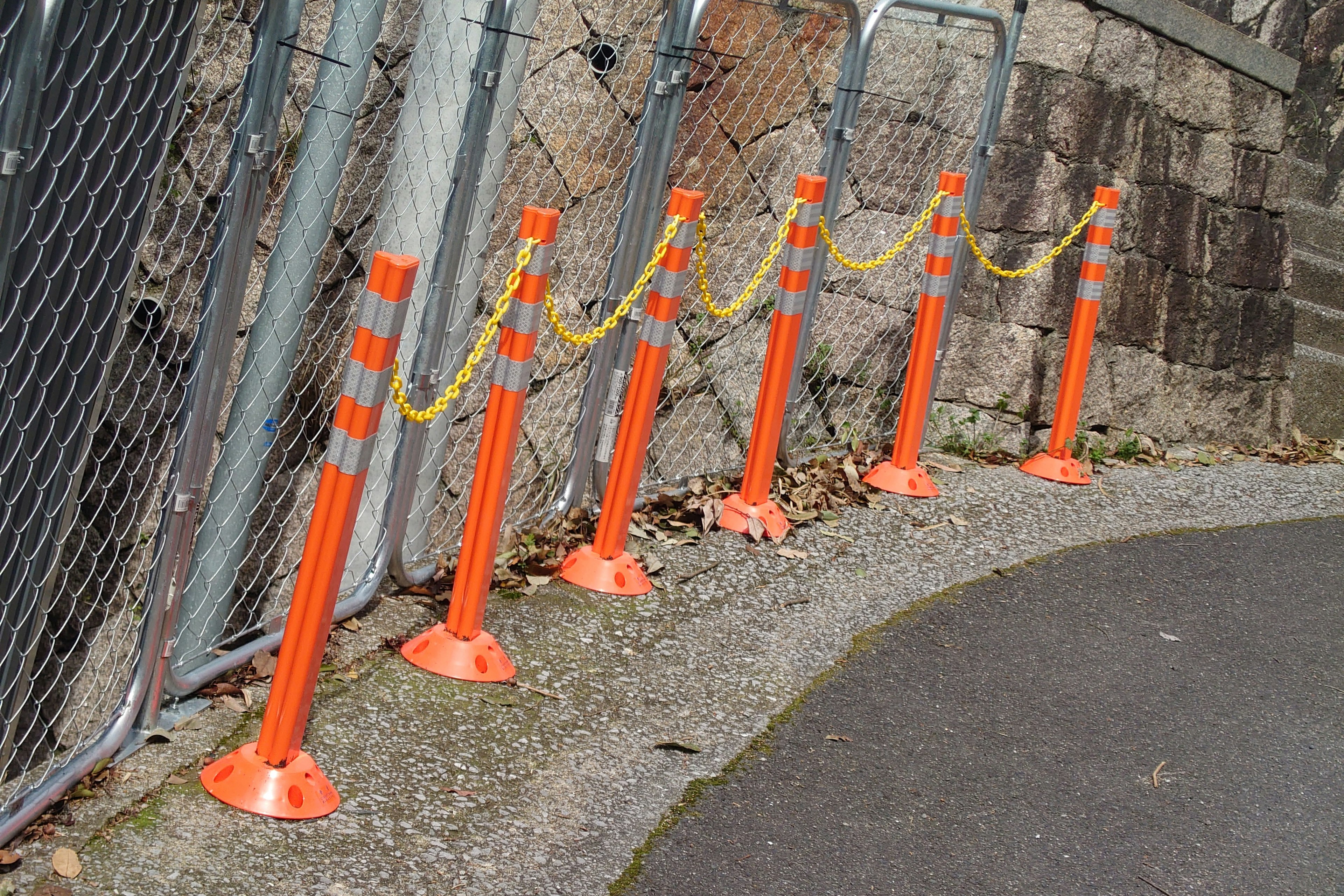 Fila de postes naranjas conectados por una cadena amarilla a lo largo de un camino