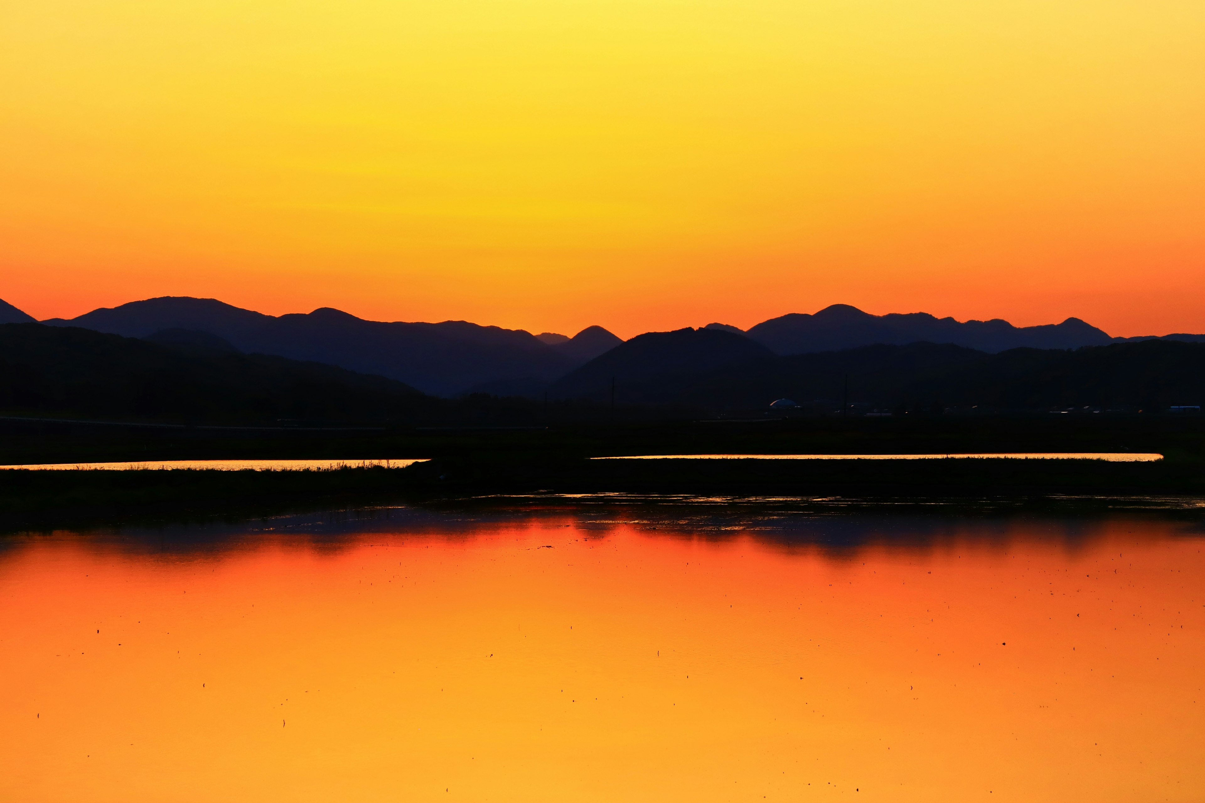 夕焼けのオレンジ色の空と山々のシルエットが映る湖の風景