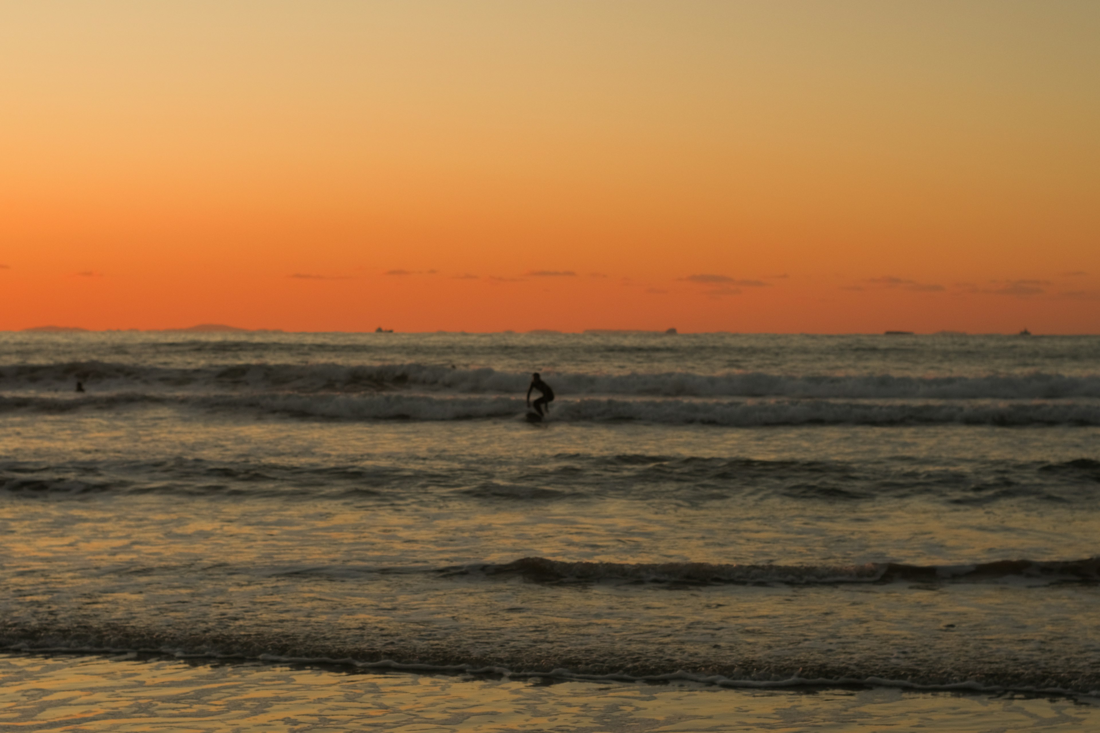 Silhouette of a surfer riding waves against a sunset backdrop