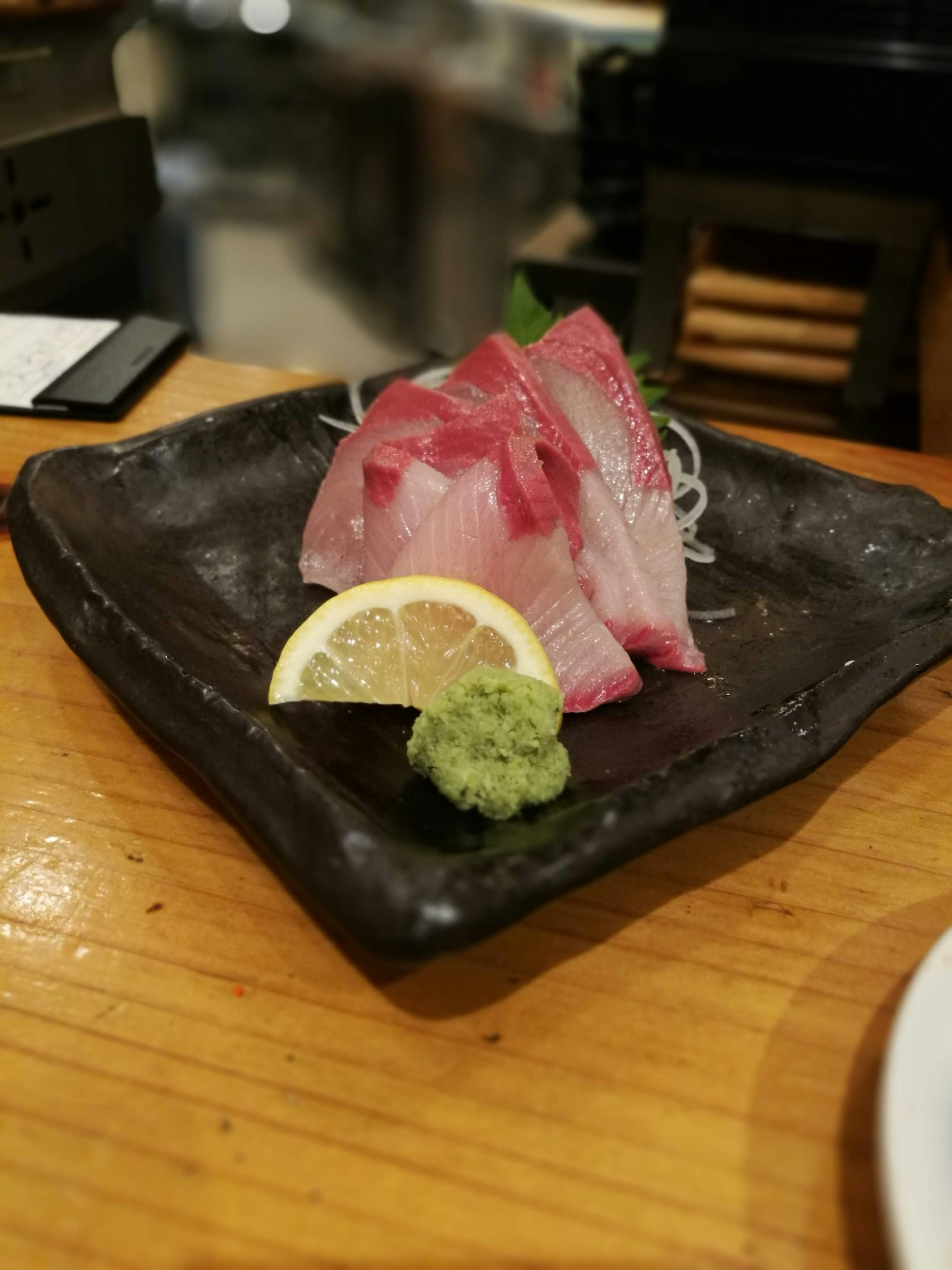 Plato de sashimi con rebanadas de pescado vibrantes servido con limón y wasabi en un plato negro