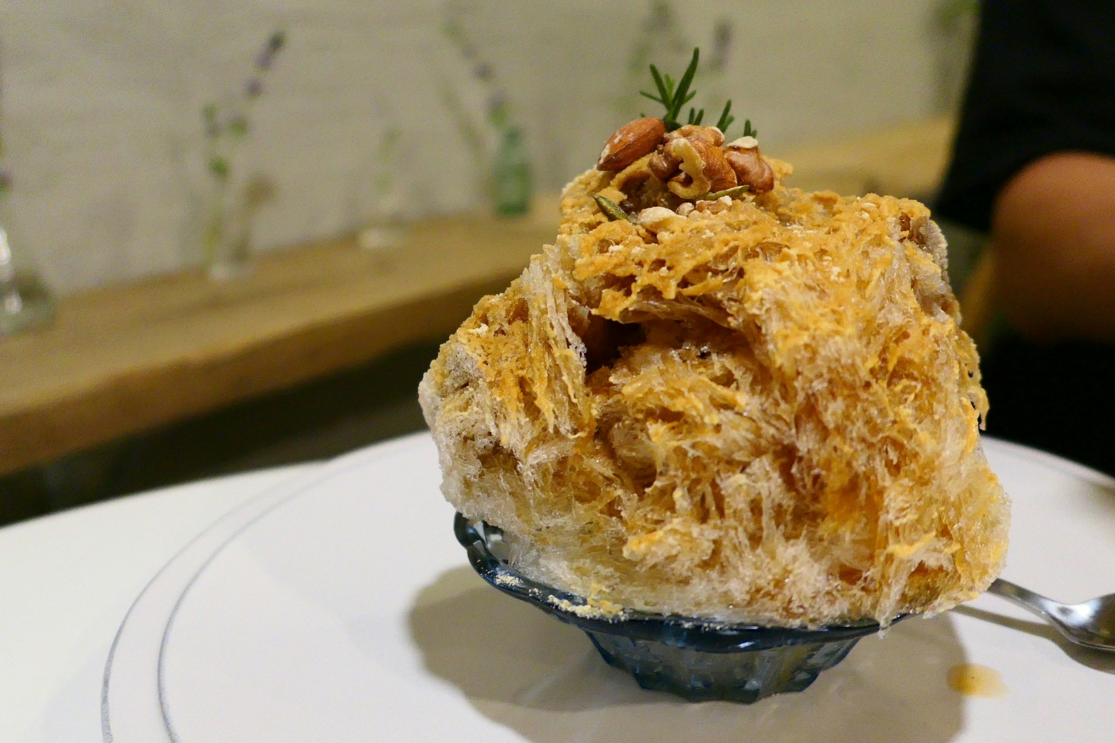 Fluffy shaved ice in a black bowl topped with caramel sauce and nuts