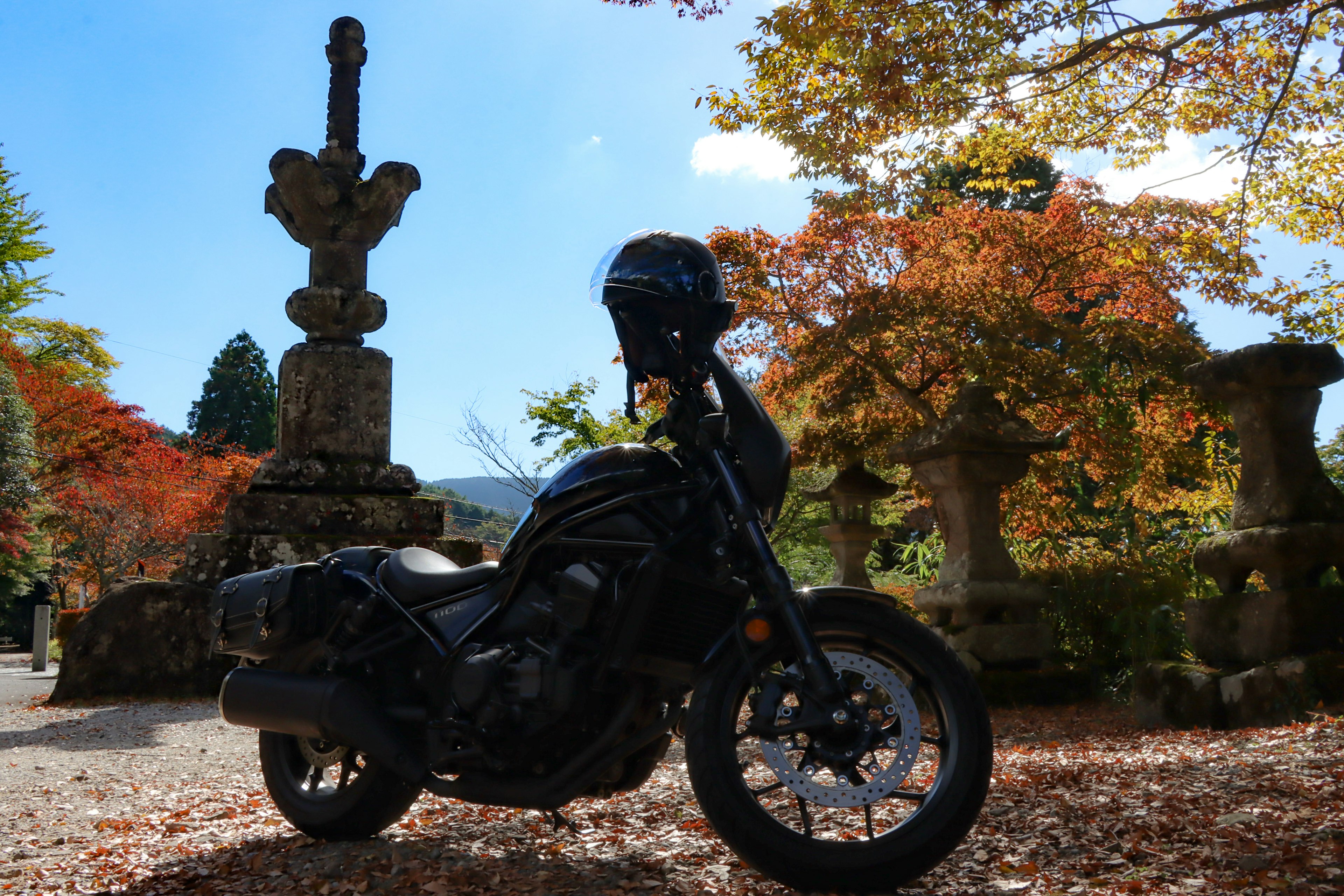 Motocicleta negra situada entre el follaje otoñal con monumentos de piedra