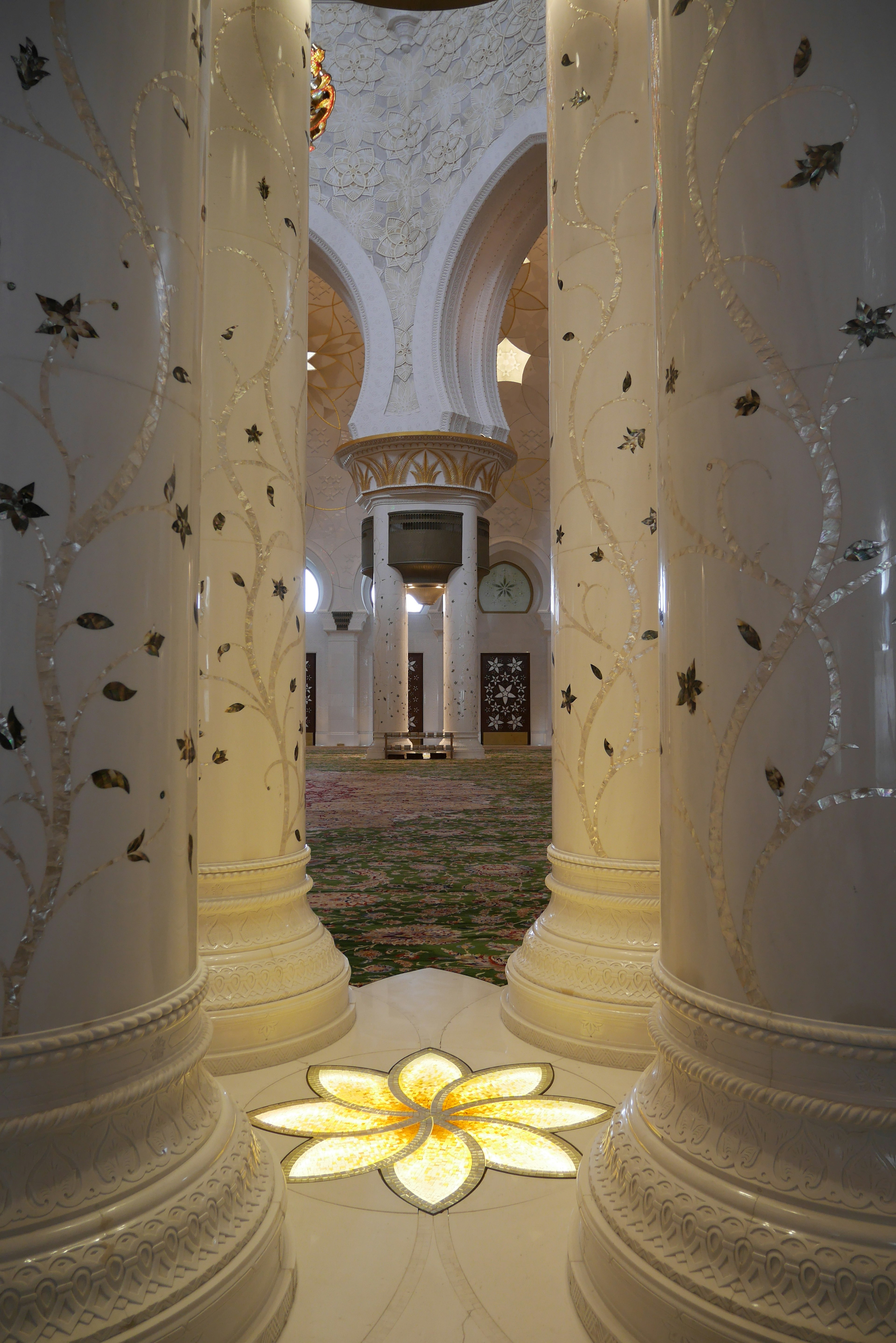 Interior view featuring white columns with gold decorations illuminated by a glowing flower design on the floor