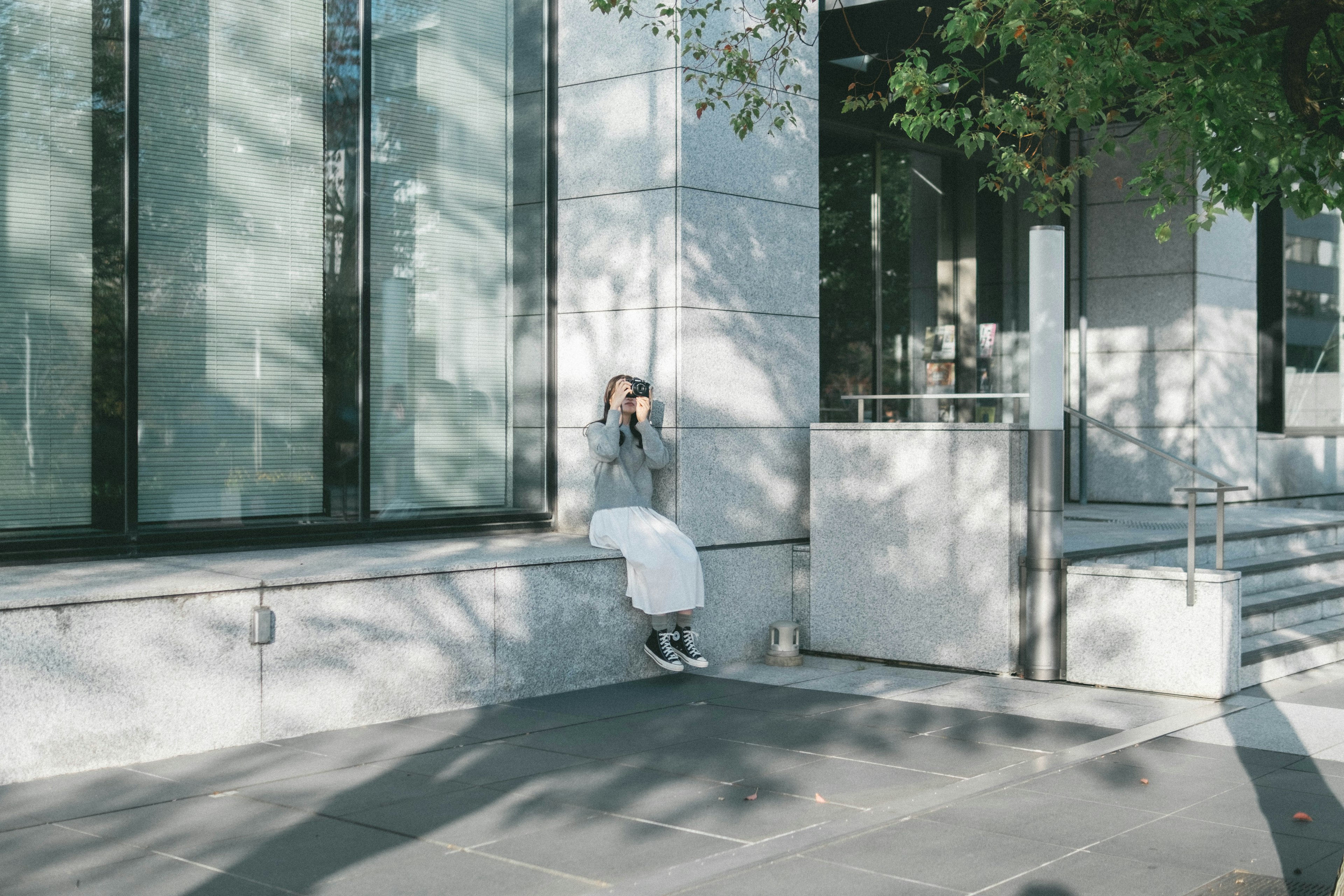 A woman sitting in front of a modern building with striking light and shadow contrasts