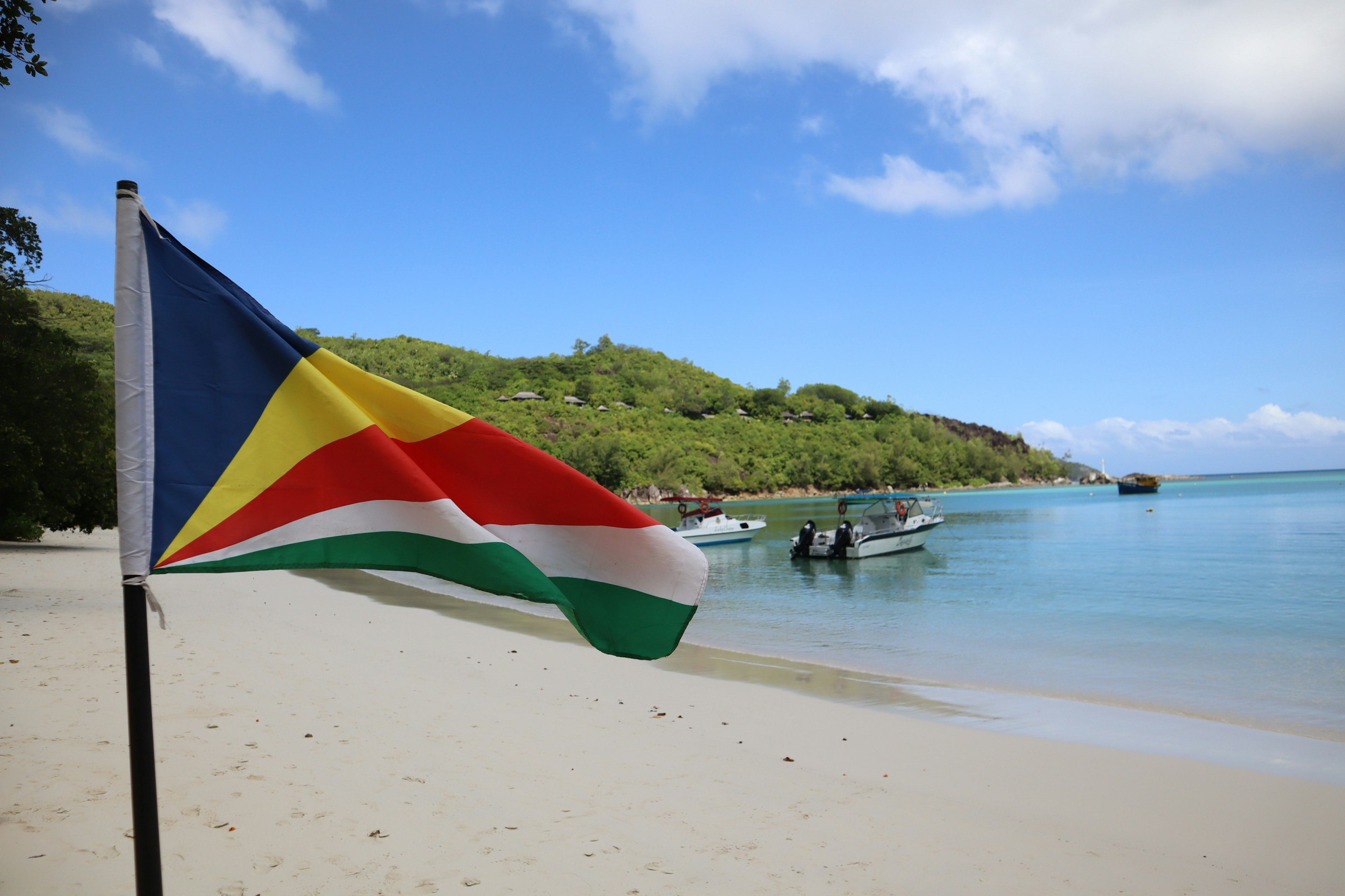 Seychelles flag waving on the beach with boats in the background