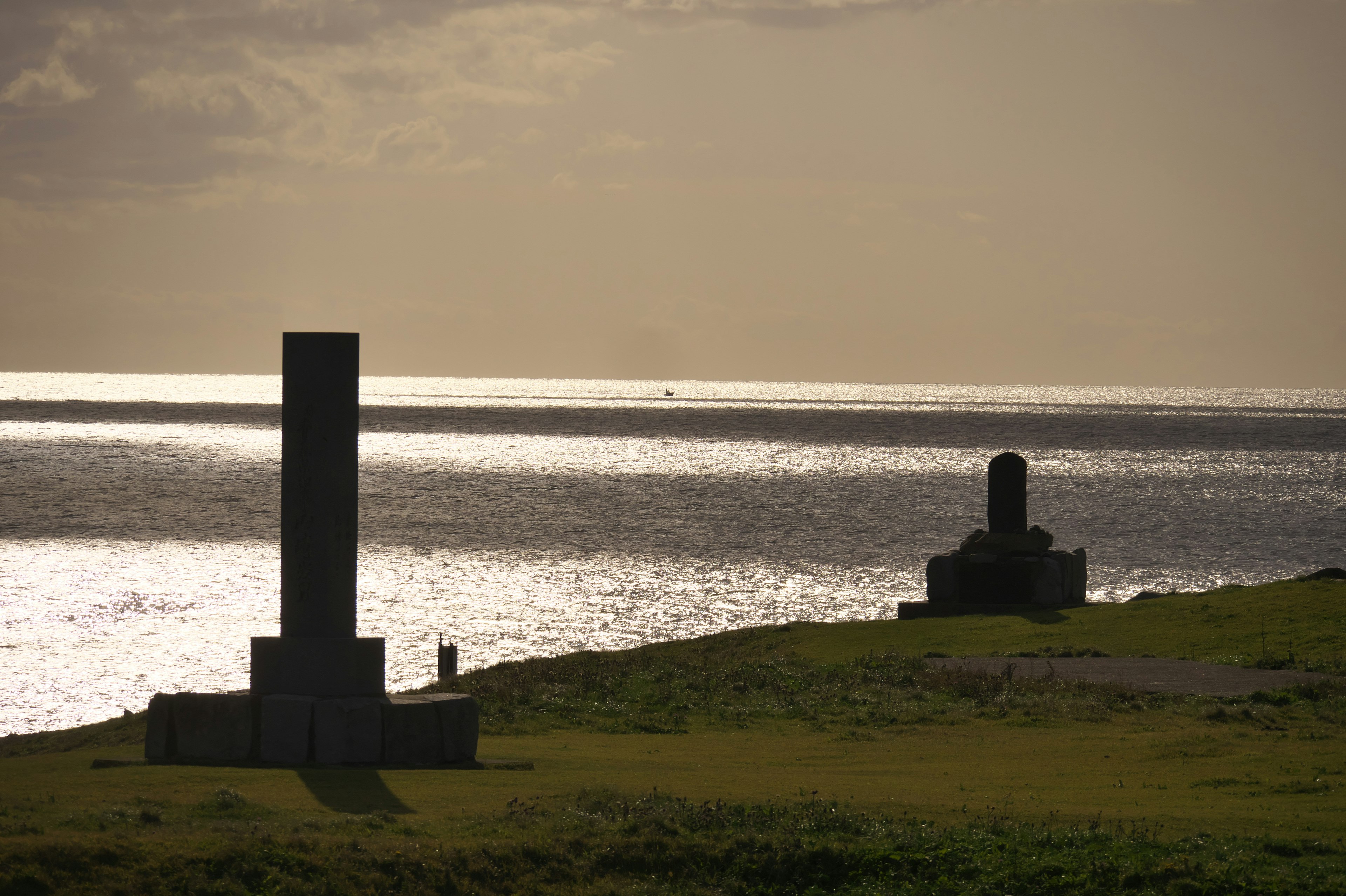 Due sculture di pietra su terreno erboso che si affacciano sul mare al tramonto