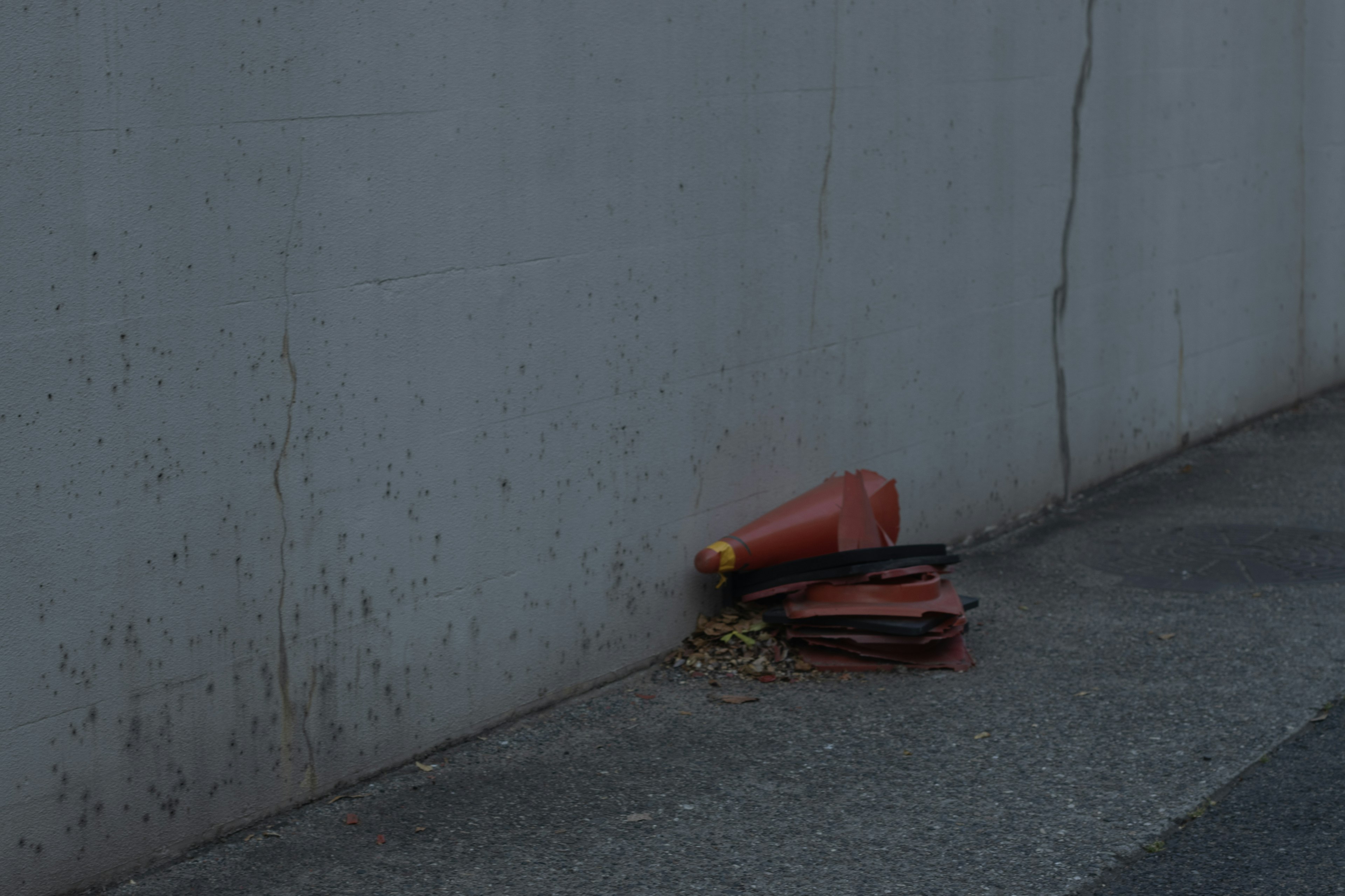 Cono de tráfico rojo y manguera negra apoyados contra una pared gris