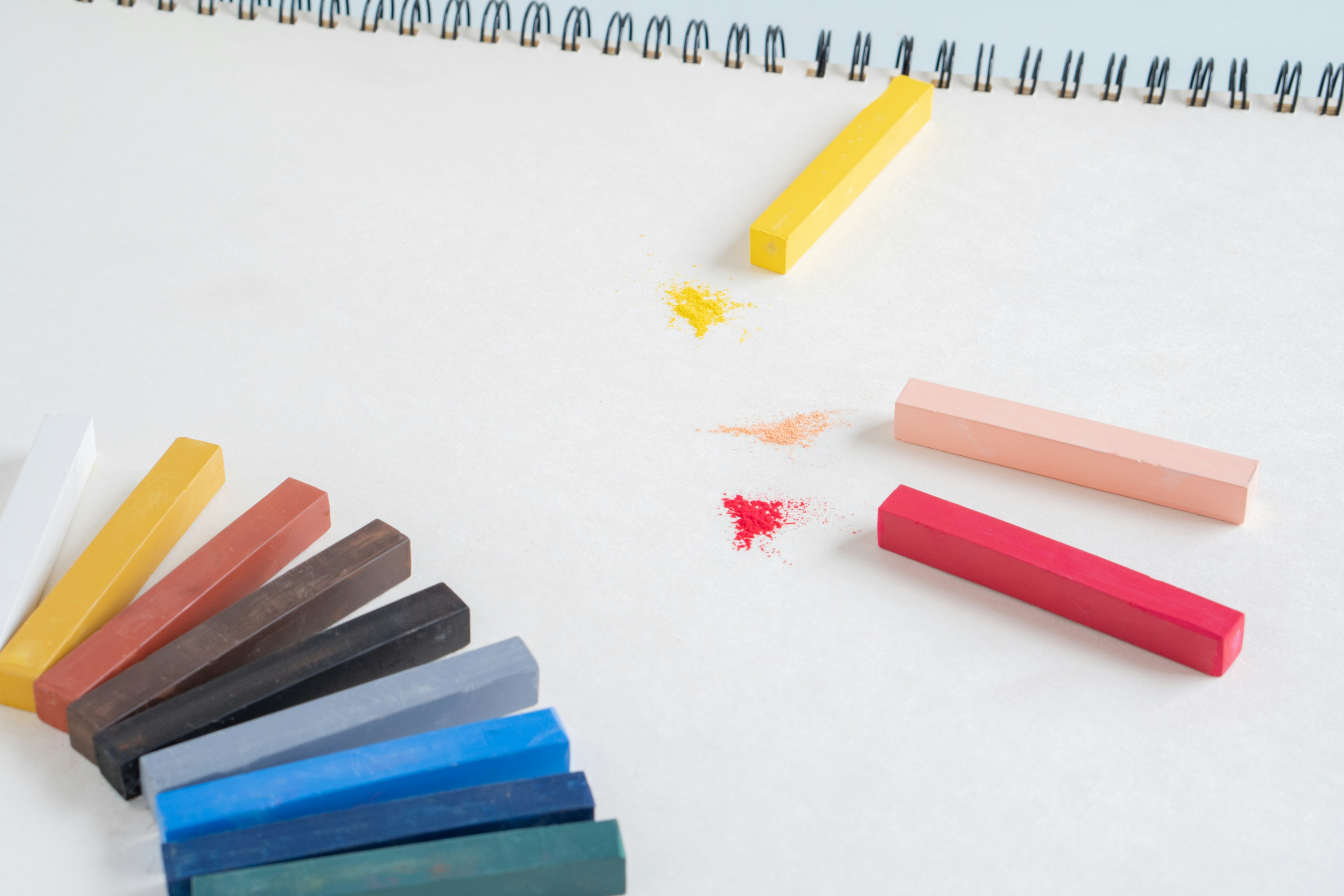 Colorful crayons arranged beside a sketchbook on a white background