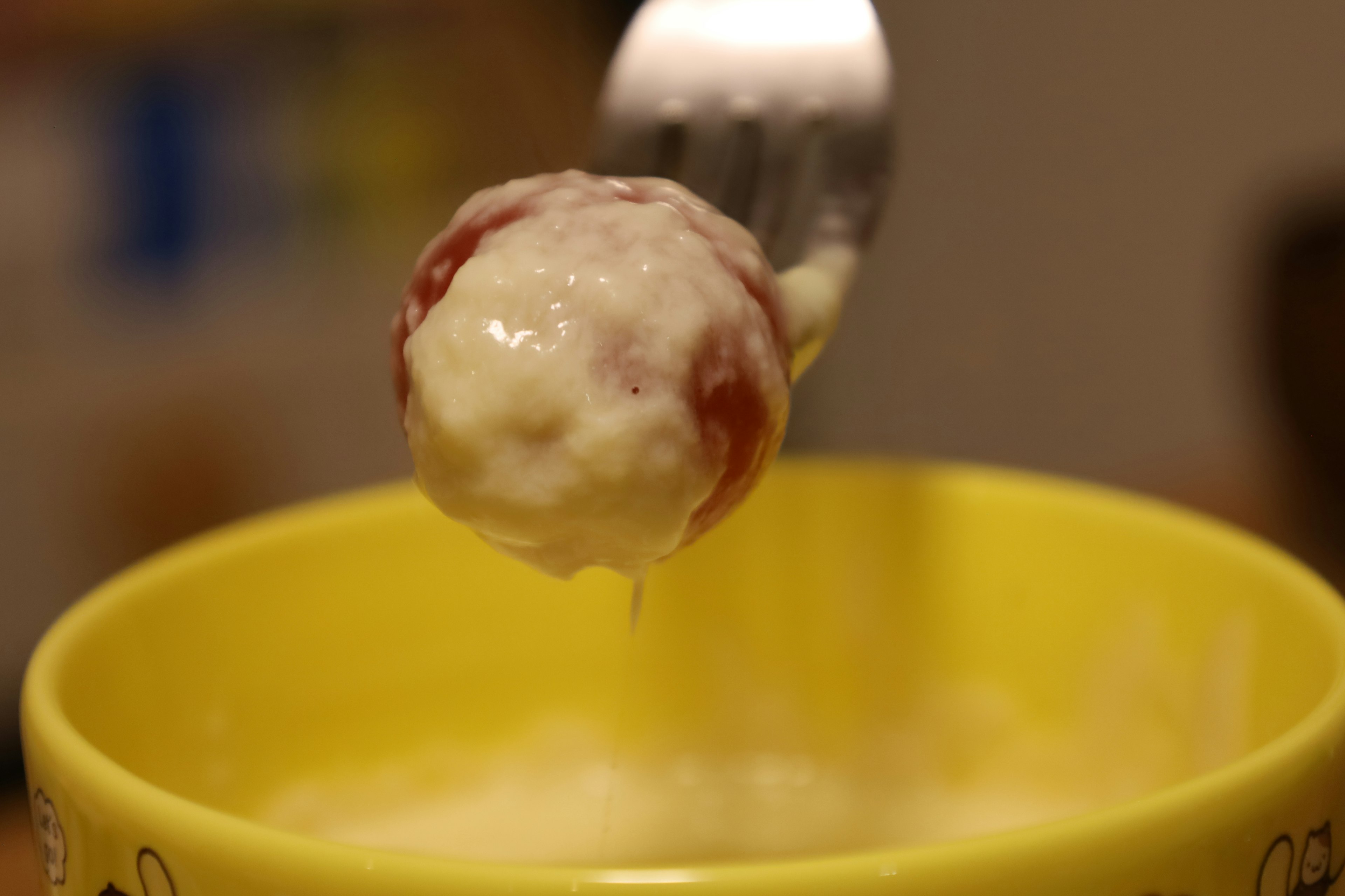 Une fourchette soulevant une boule de viande rouge au-dessus d'un bol jaune rempli de sauce crémeuse