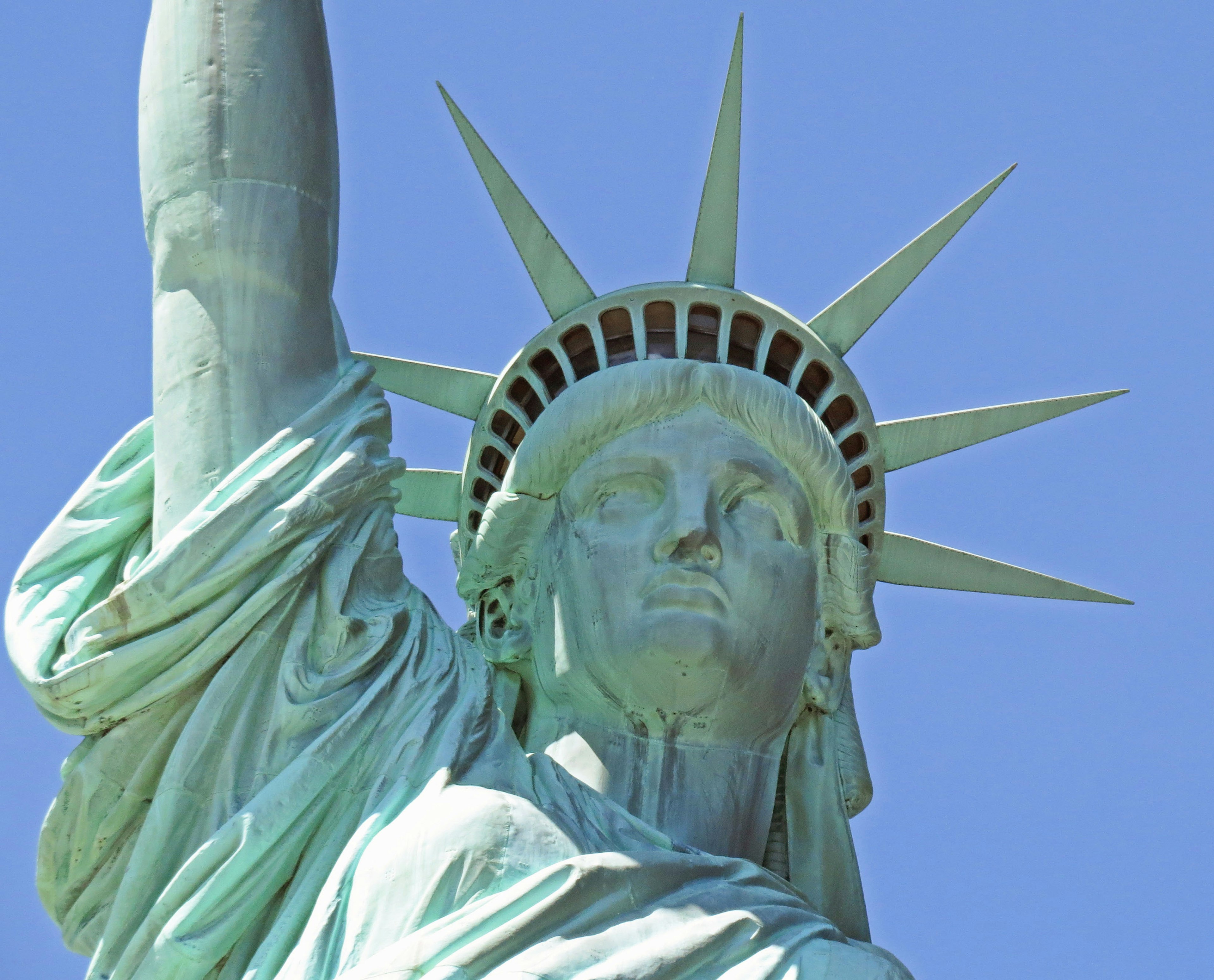 Gros plan sur le visage et la couronne de la Statue de la Liberté sous un ciel bleu clair