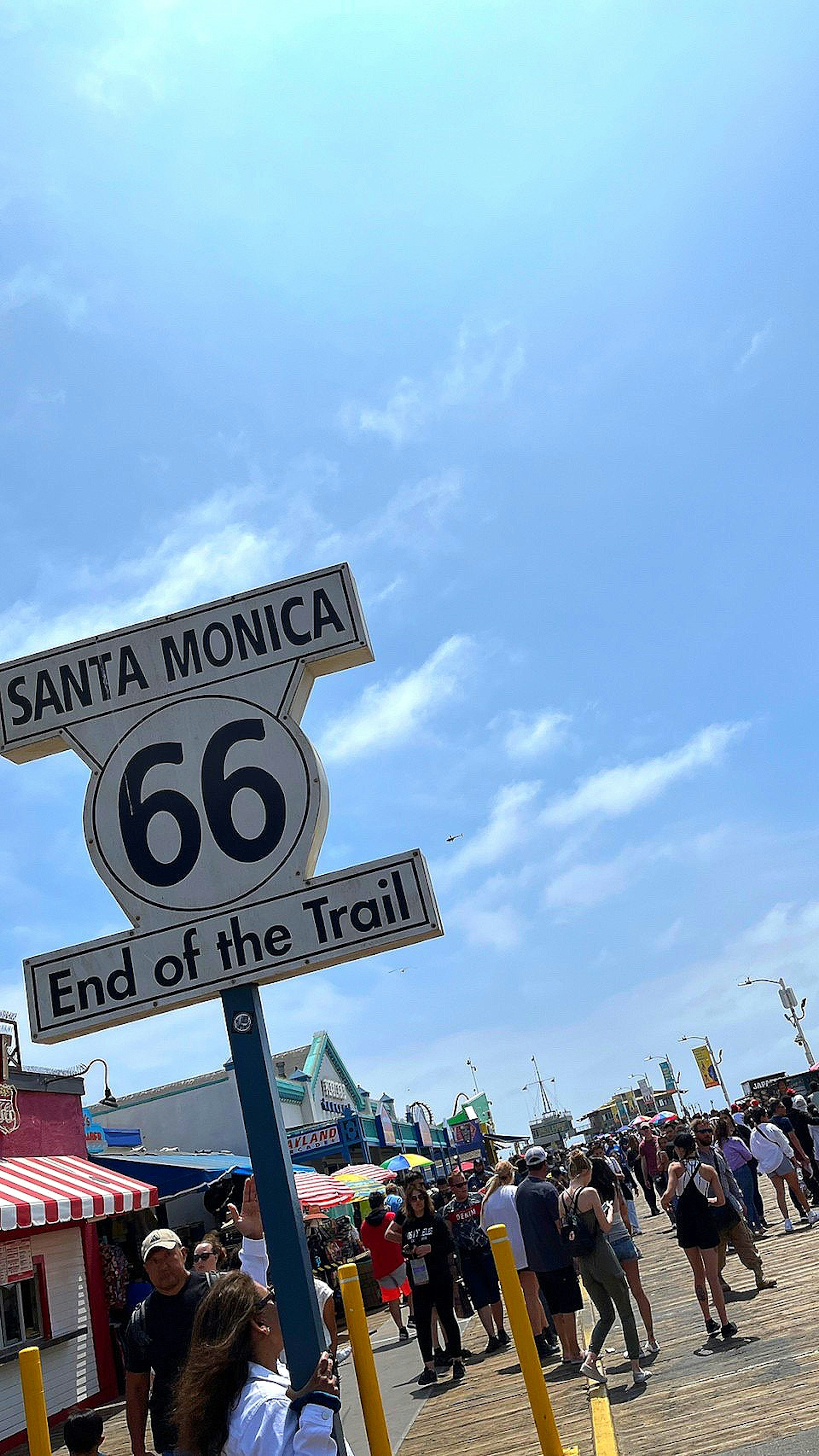 Route 66 Schild in Santa Monica mit Menschenmenge am Strand