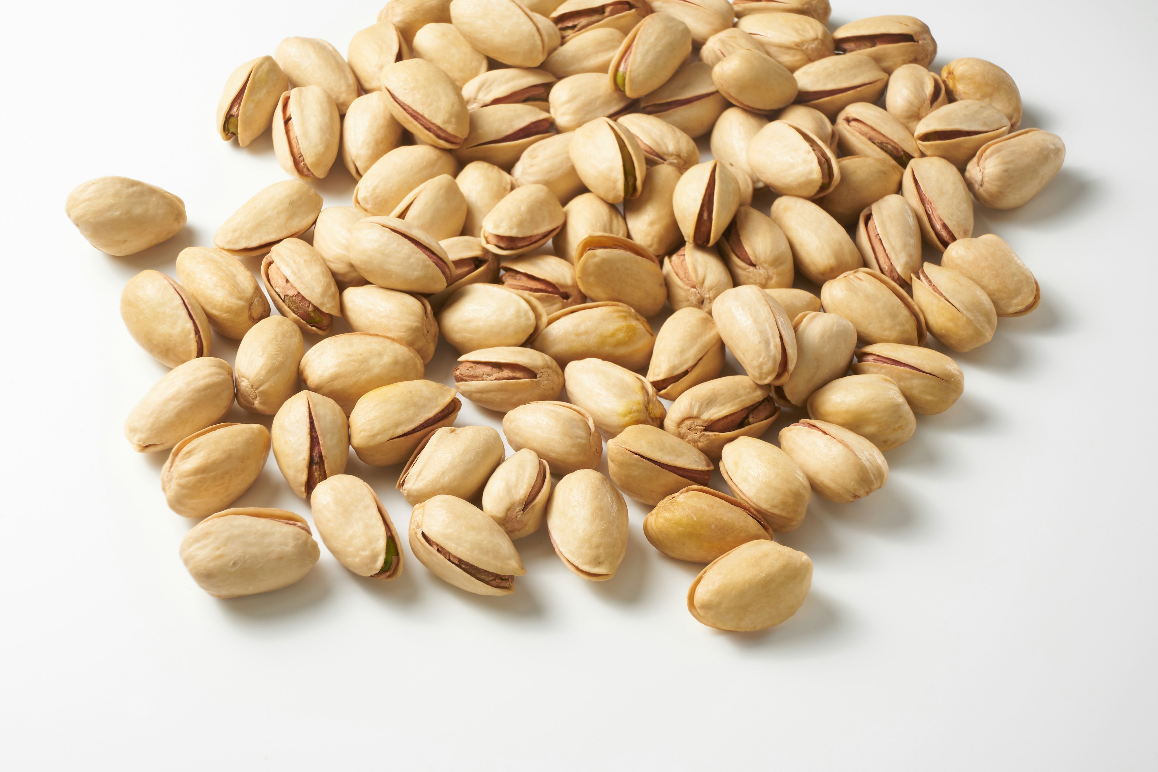 A pile of unshelled pistachios scattered on a white surface