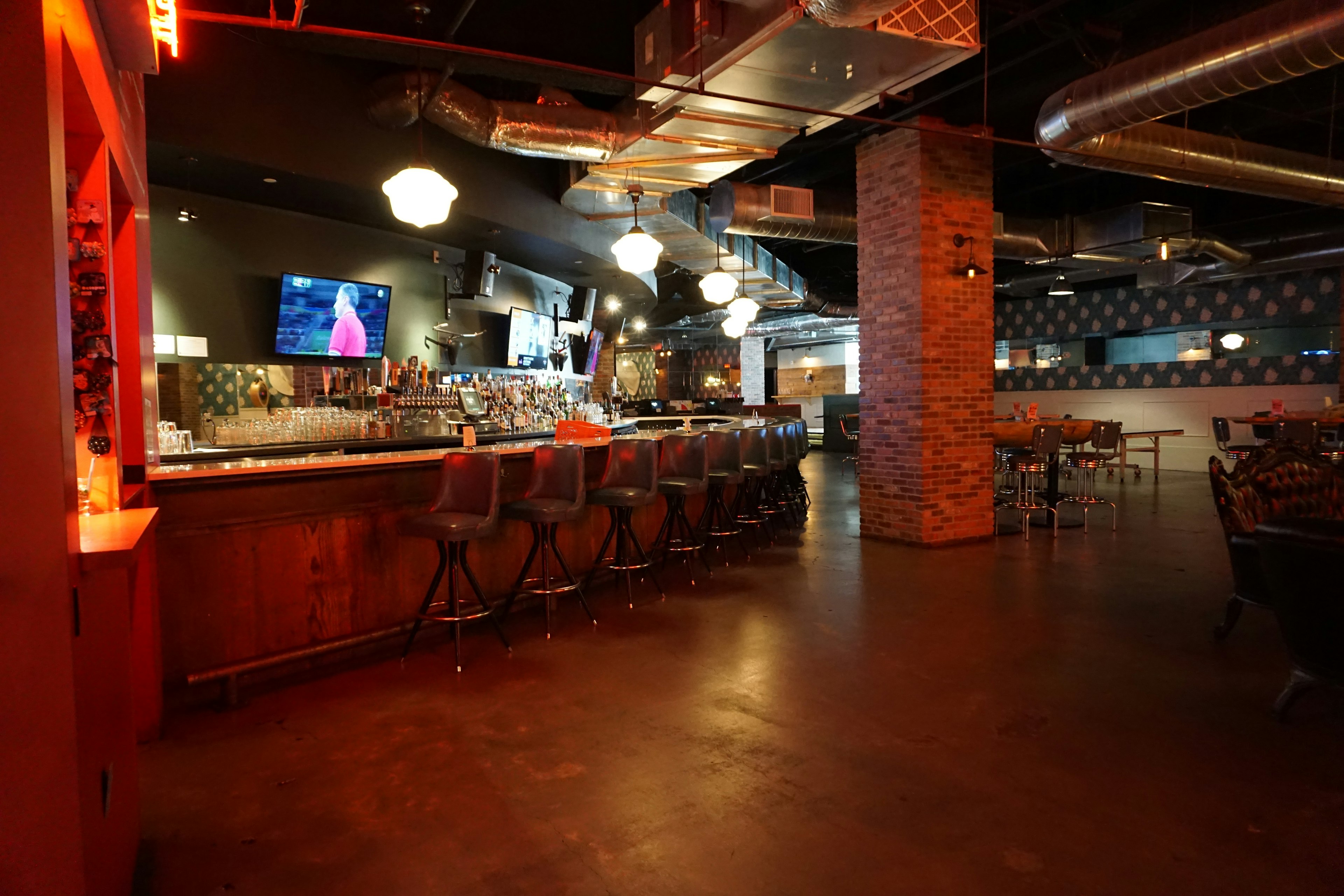 Interior de bar moderno con mostrador de madera iluminación roja pared de ladrillo expuesto y una televisión