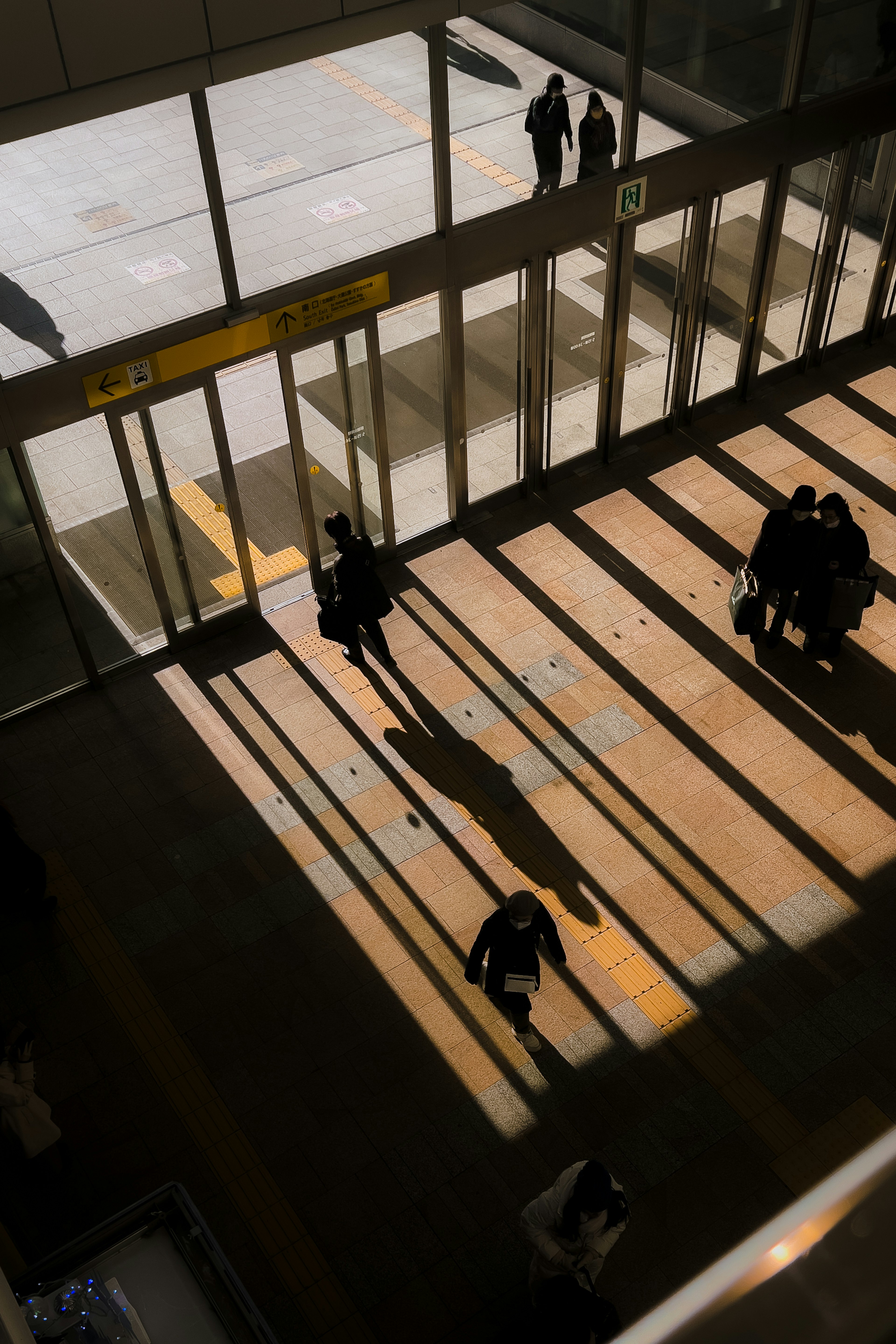 People casting shadows while moving through a bright entrance