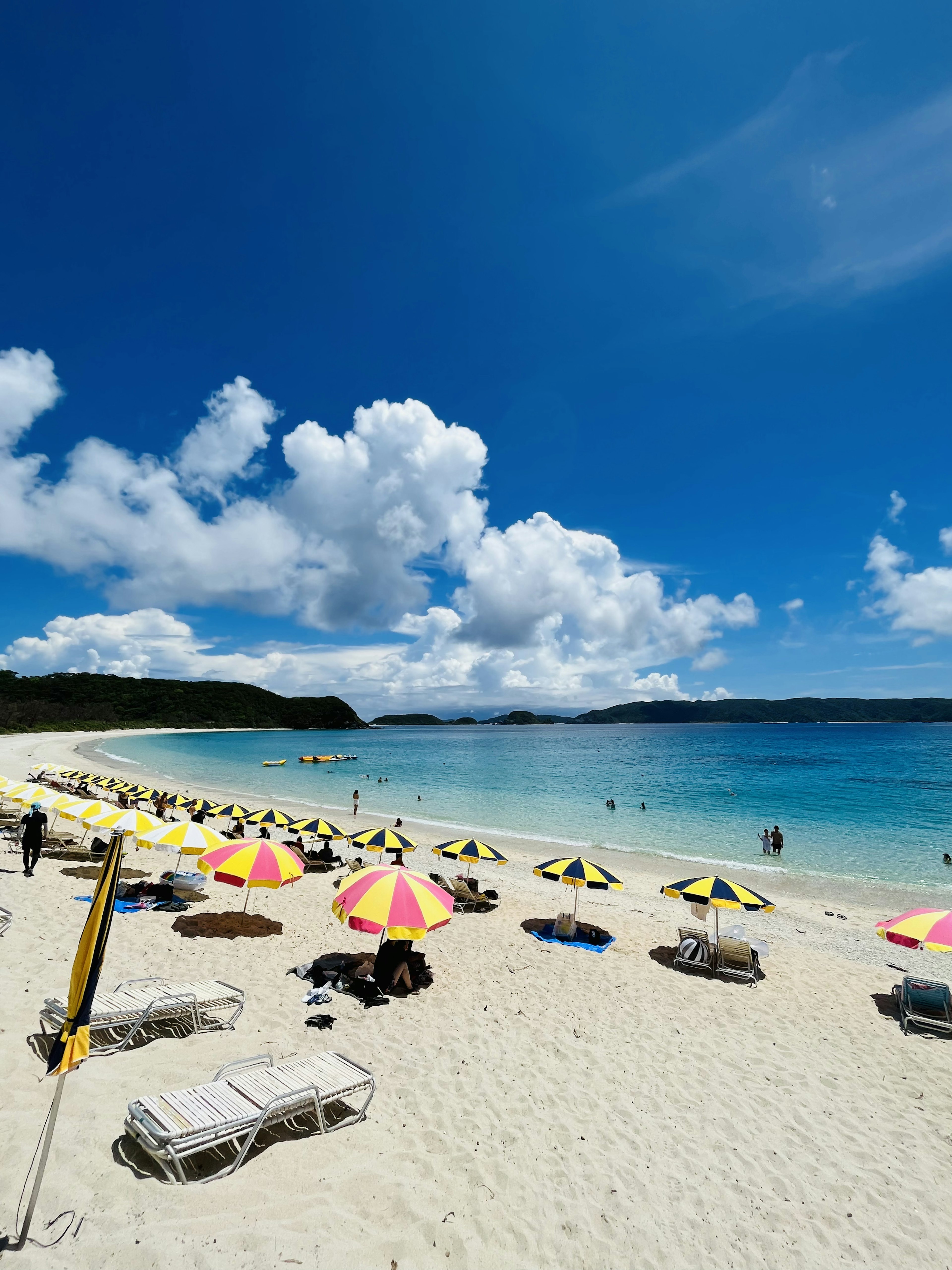 Una spiaggia con ombrelloni colorati e lettini su sabbia bianca accanto a un mare blu chiaro