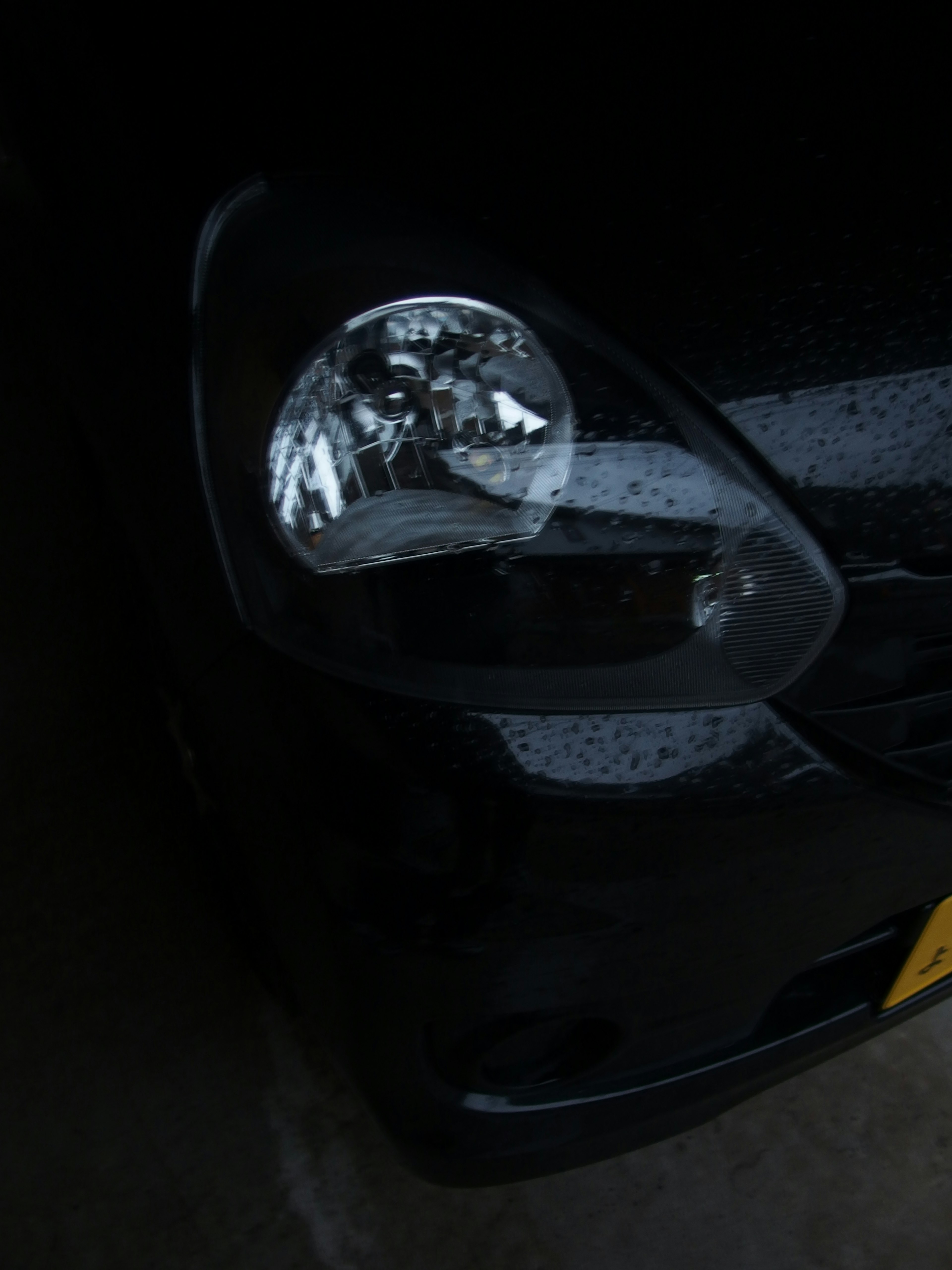 Close-up of a black car's headlight with raindrops