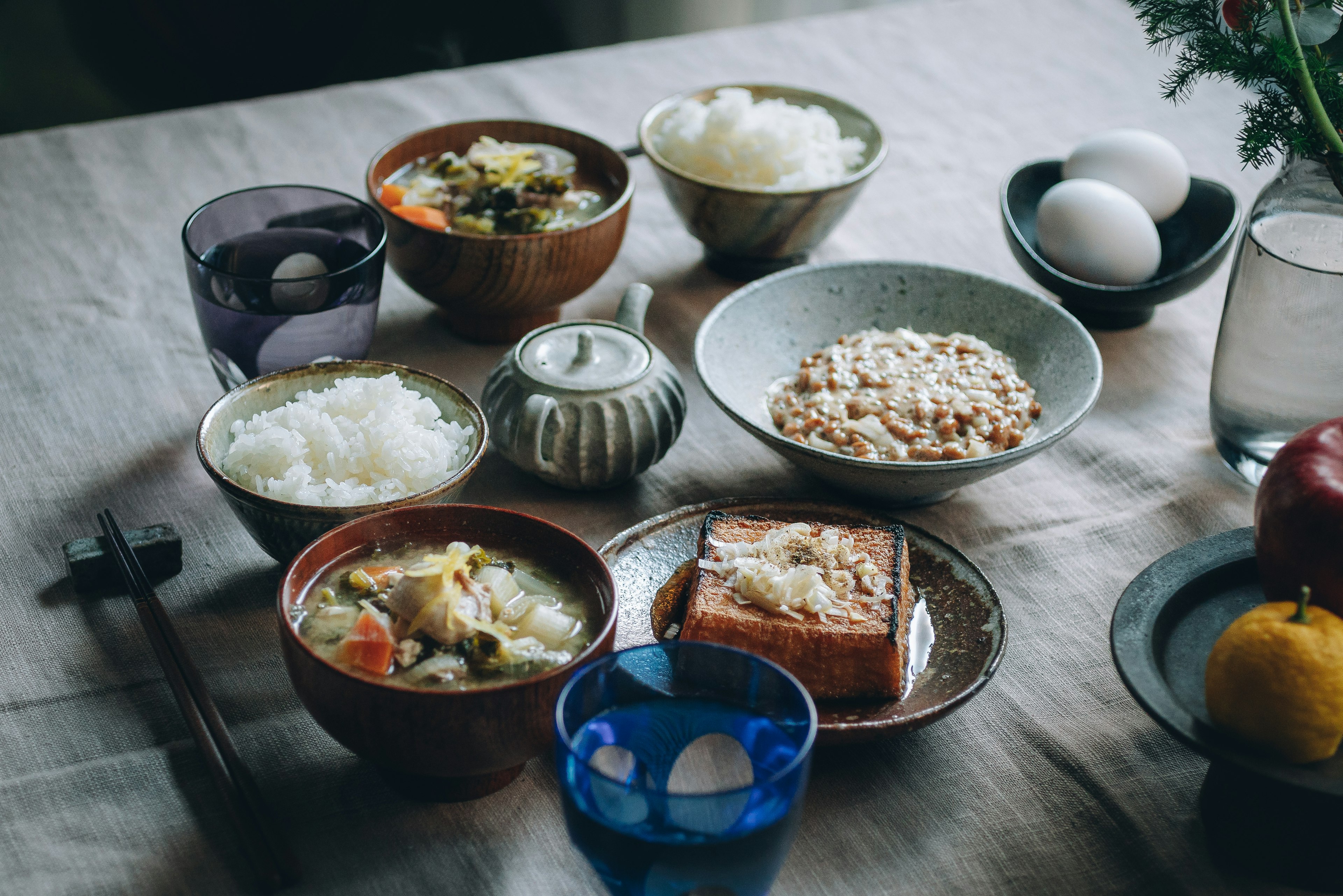 A Japanese breakfast spread with colorful bowls of rice, soup, tofu, eggs, and fruit on a table