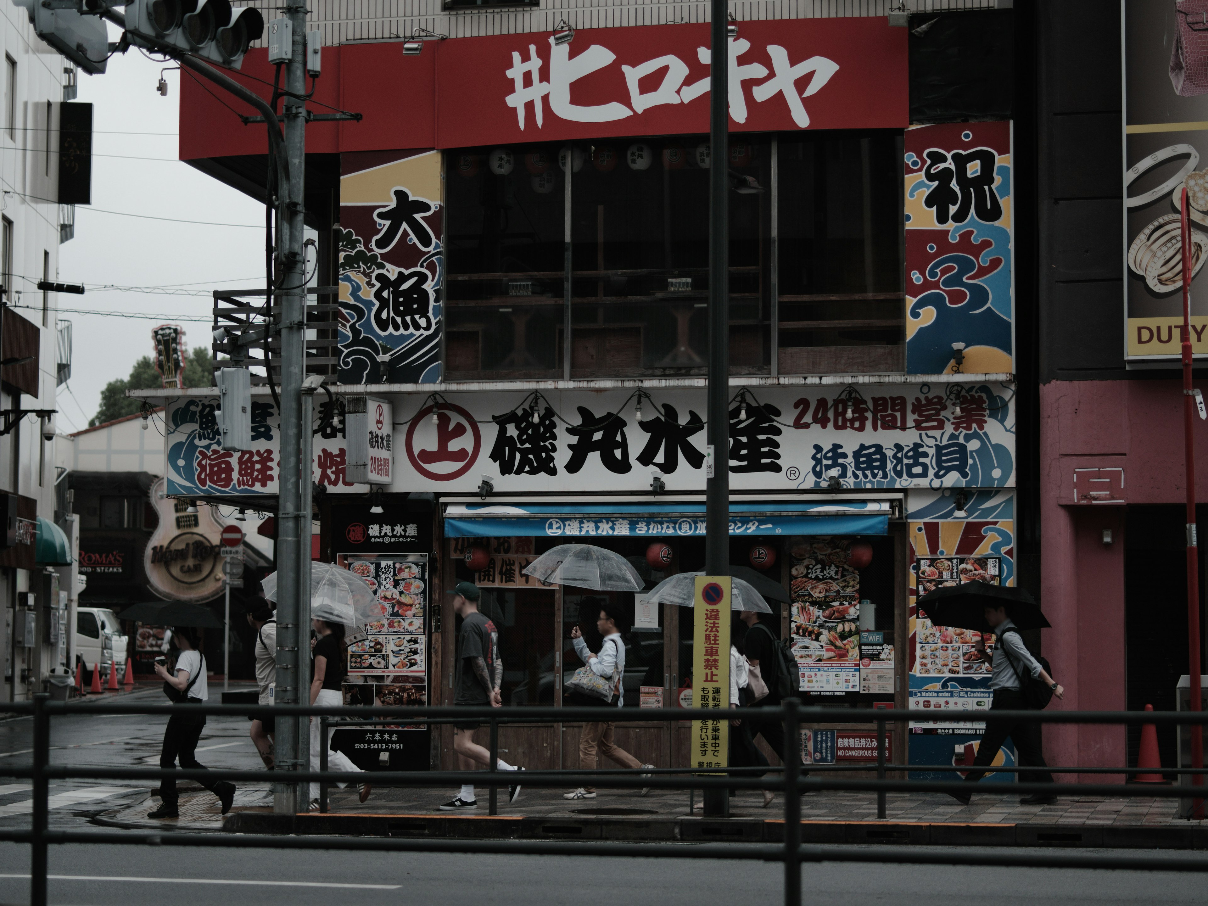 Street scene with people holding umbrellas in the rain shop signs and advertisements visible