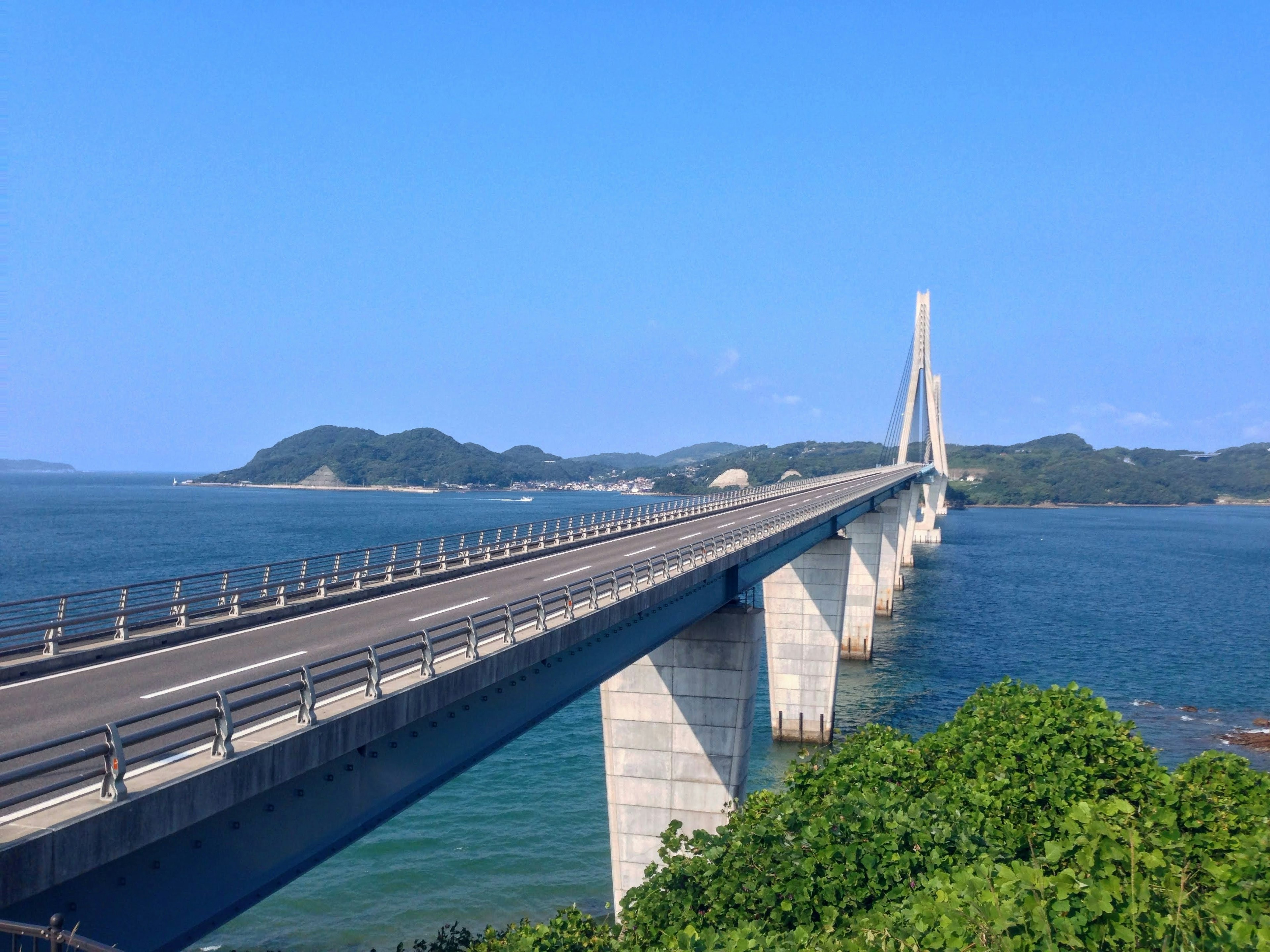 Sebuah jembatan indah yang membentang di atas laut biru dengan dedaunan hijau