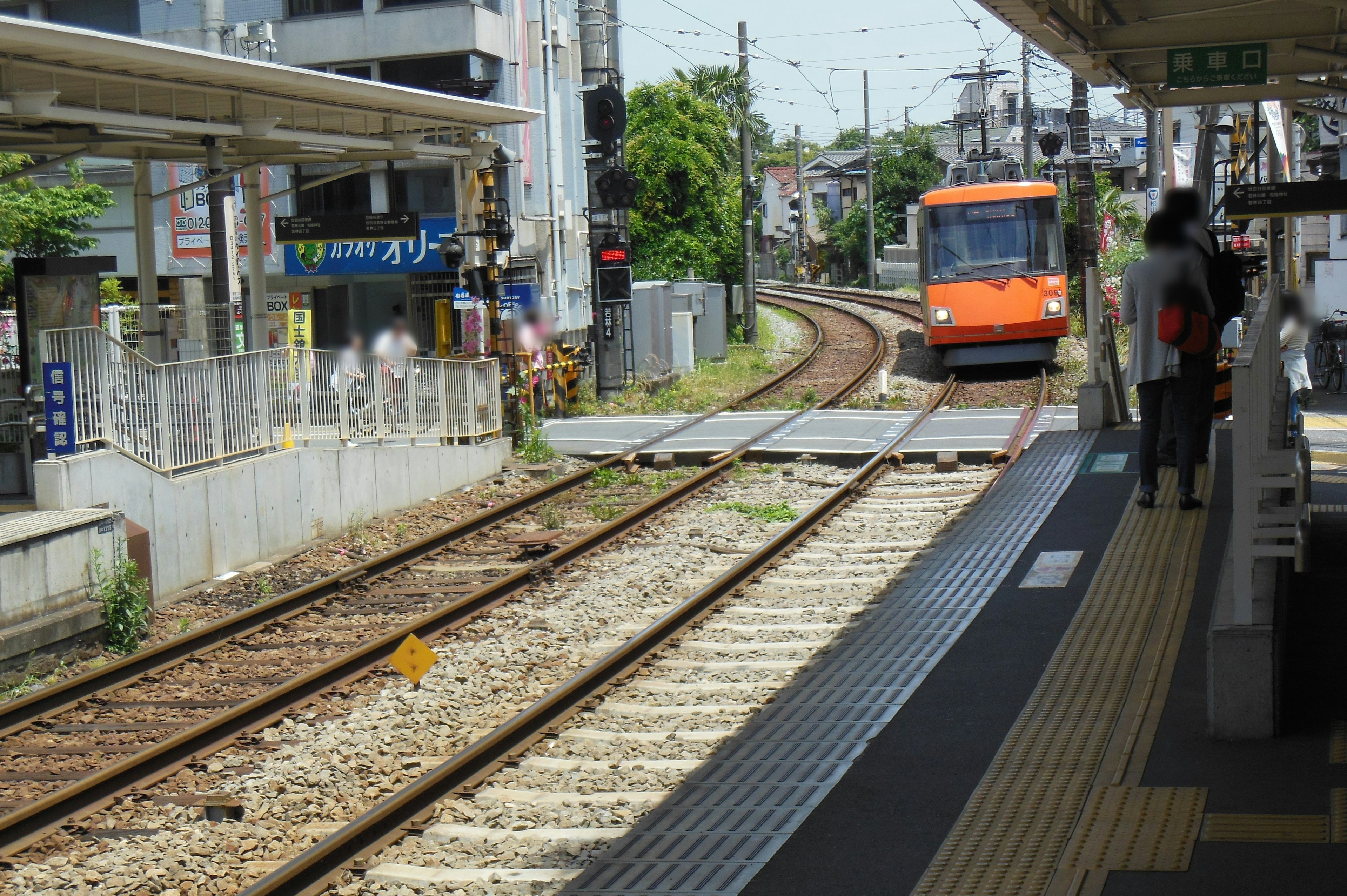 Un treno arancione che si avvicina a una curva della ferrovia in una stazione con edifici e un marciapiede