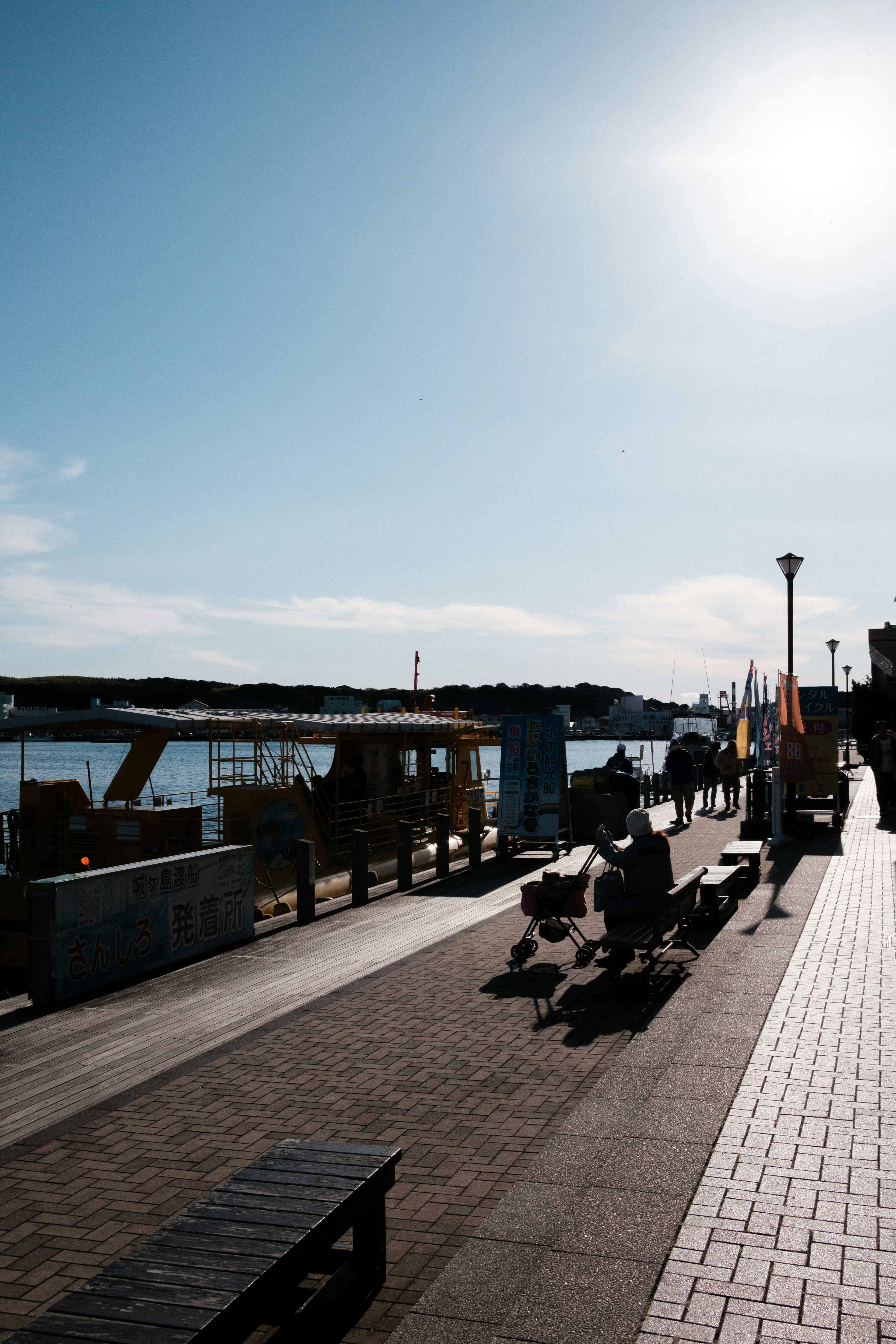 Silhouetten von Menschen, die an einem sonnigen Tag entlang einer Uferpromenade gehen